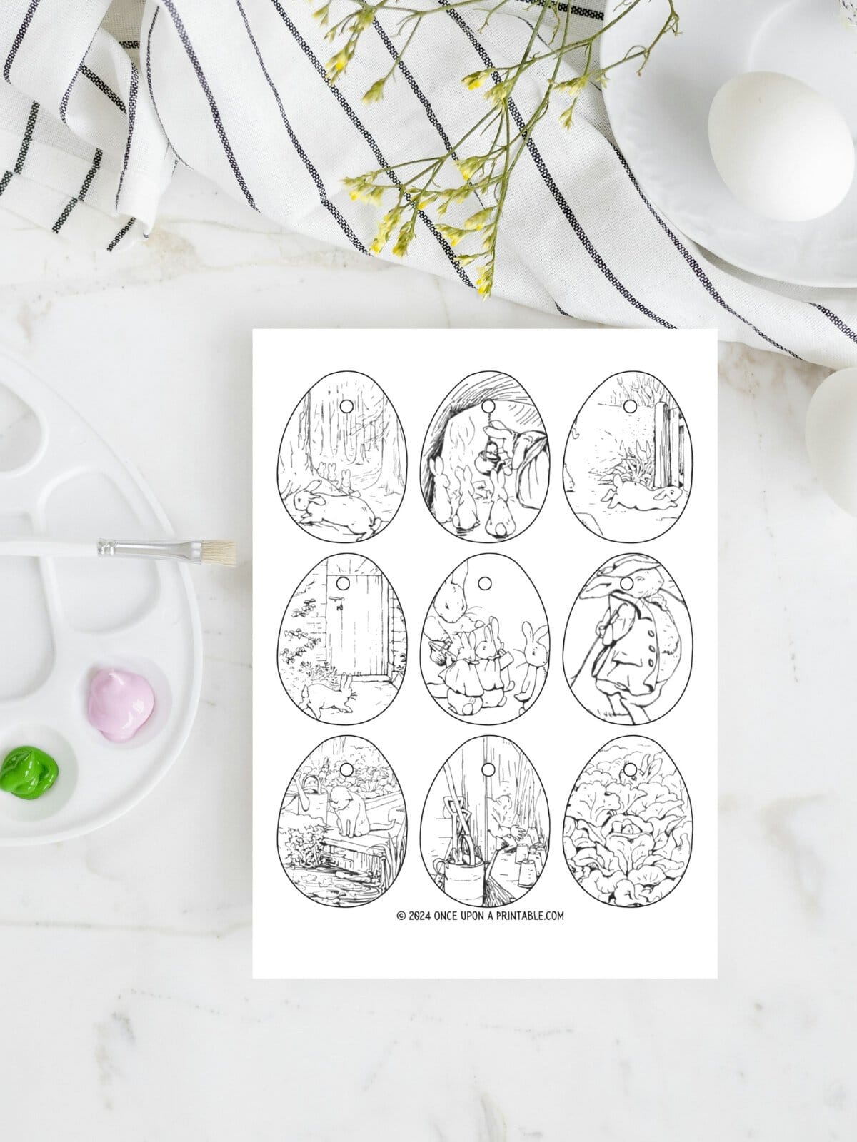 The Tale of Peter Rabbit Easter Egg coloring pages laying on a marbletop with a kitchen towel and painting.