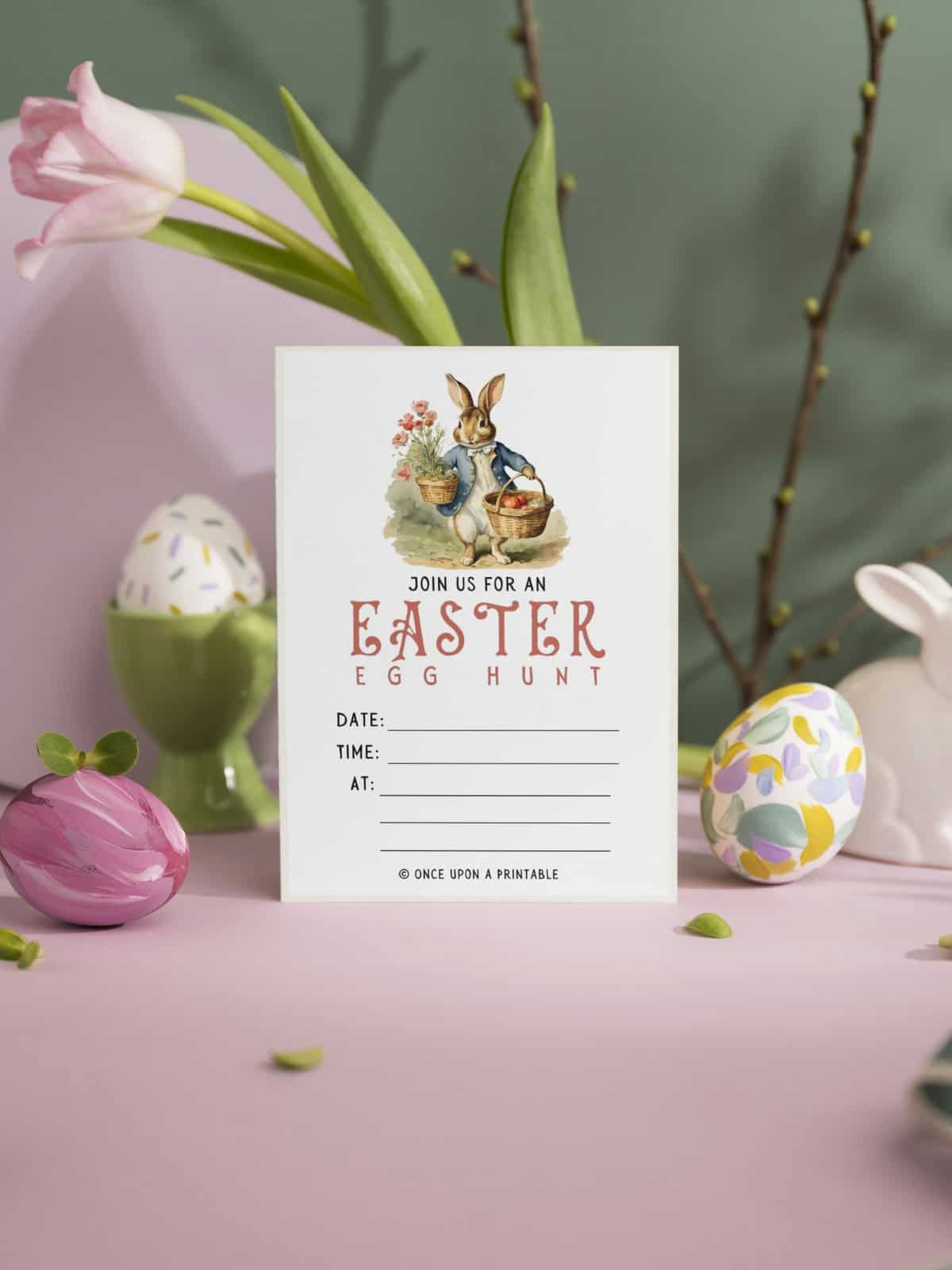 Easter egg hunt invitation Peter Rabbit inspired sitting on a pink tabletop with easter eggs.