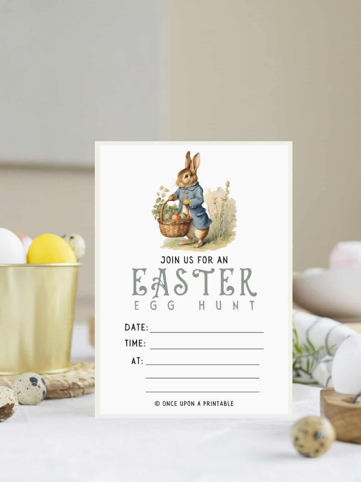 Peter Rabbit holding a basket full of tomatoes on an easter egg hunt invitation laying on a white table.