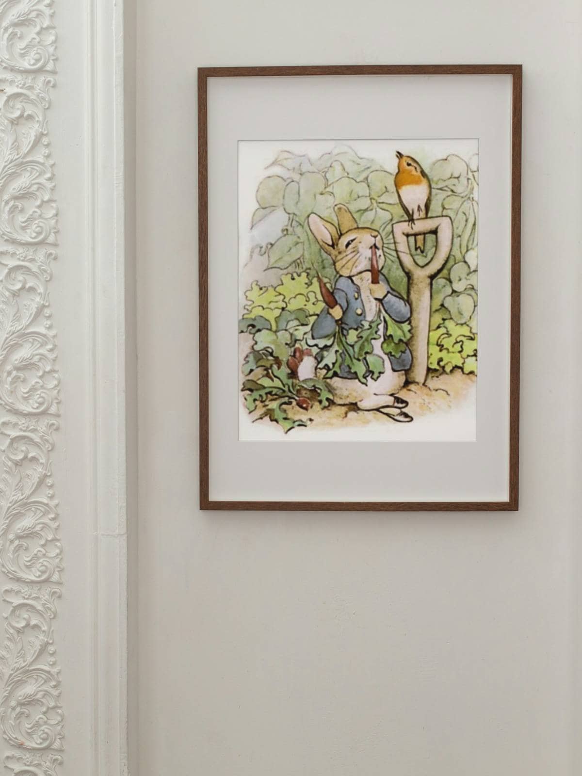 Peter Rabbit munching on radishes in Mr McGregor's garden art print hanging on a white wall.