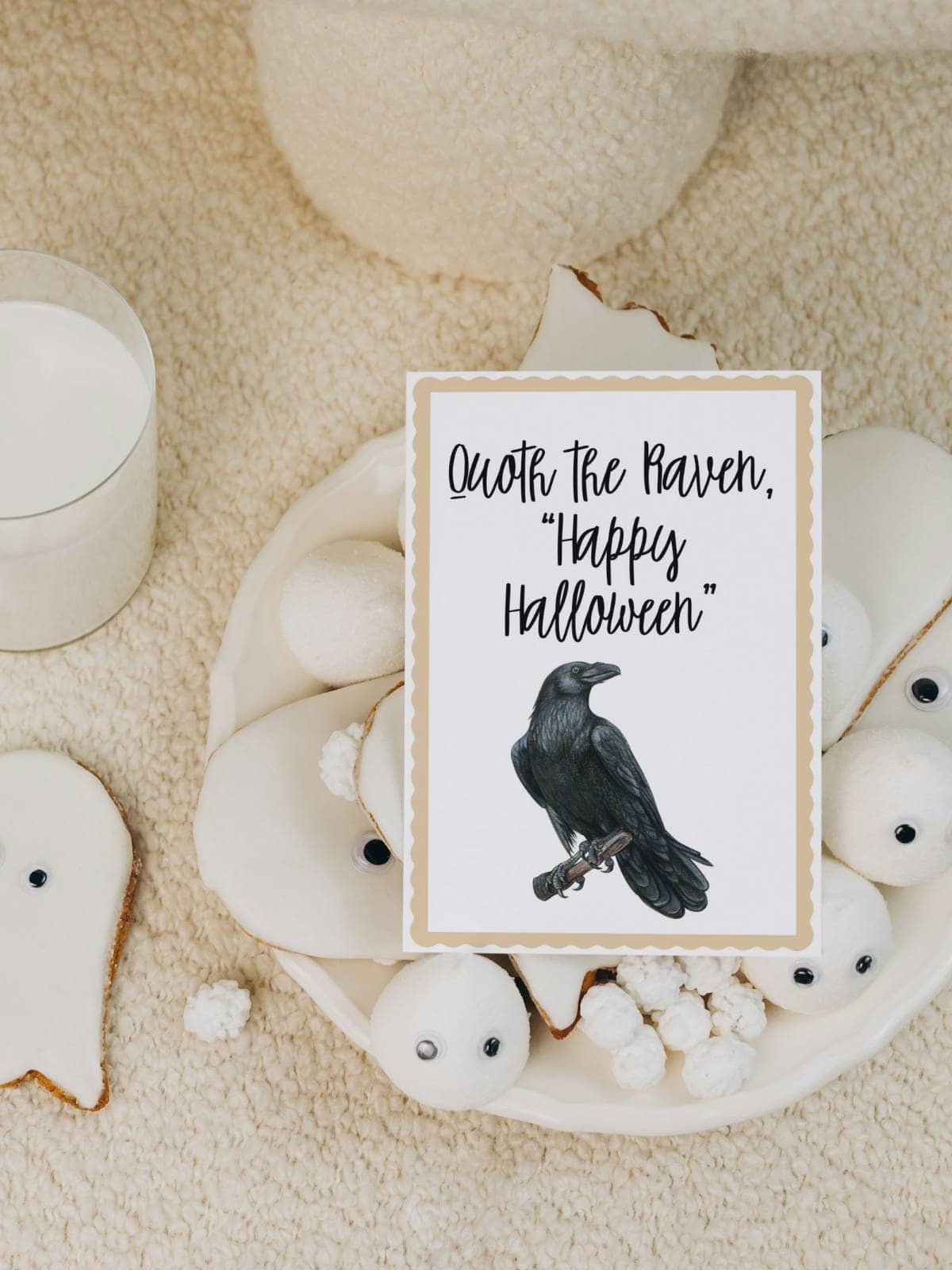 A Raven on a Halloween notecard sitting on top of a pile of ghost cookies iced with white icing.