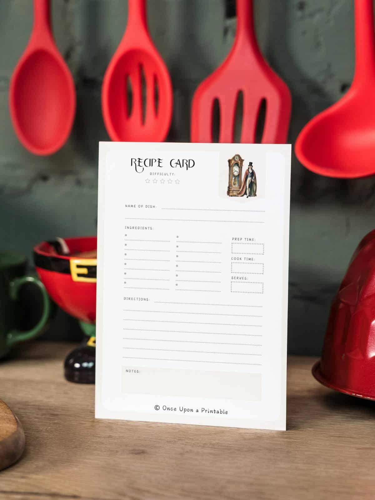 Nutcracker-themed recipe card with a godfather clock and godfather Drosselmeier, sitting in front of red kitchen utensils on a countertop.