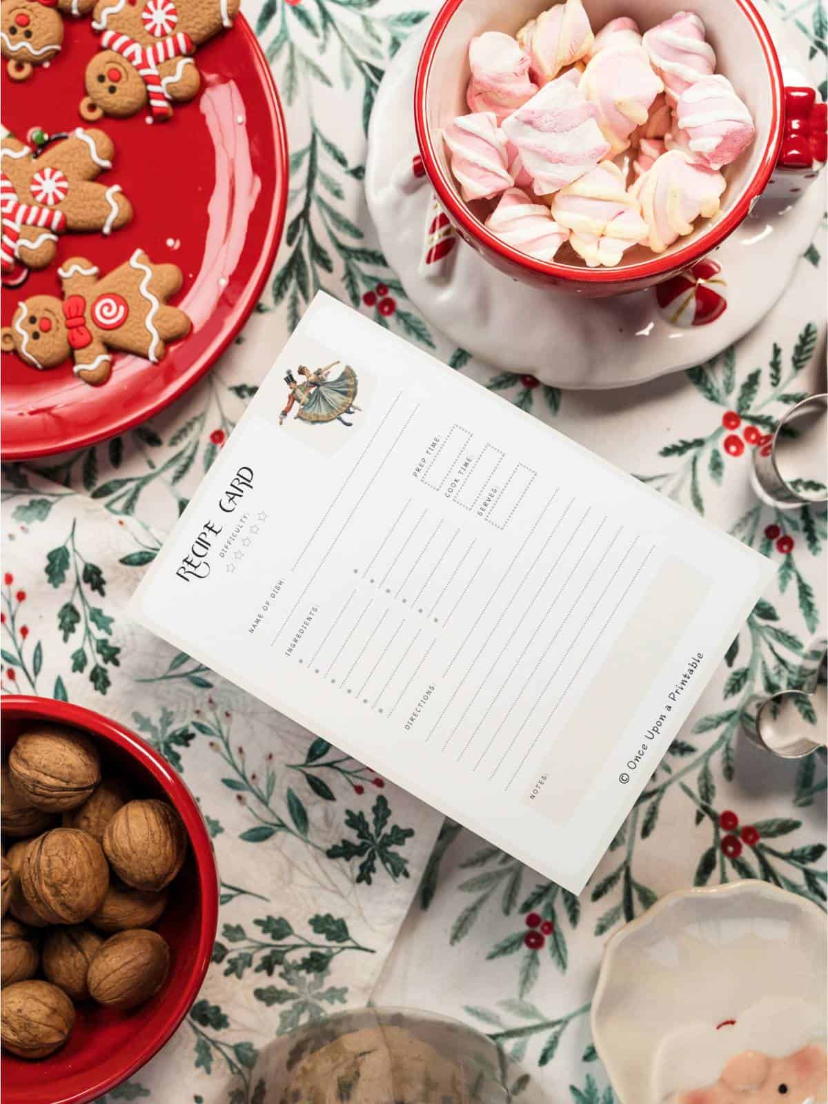Nutcracker-themed recipe card sitting on a table with candy cane treats, gingerbread cookies, and cookie balls in holiday themed plates and bowls.
