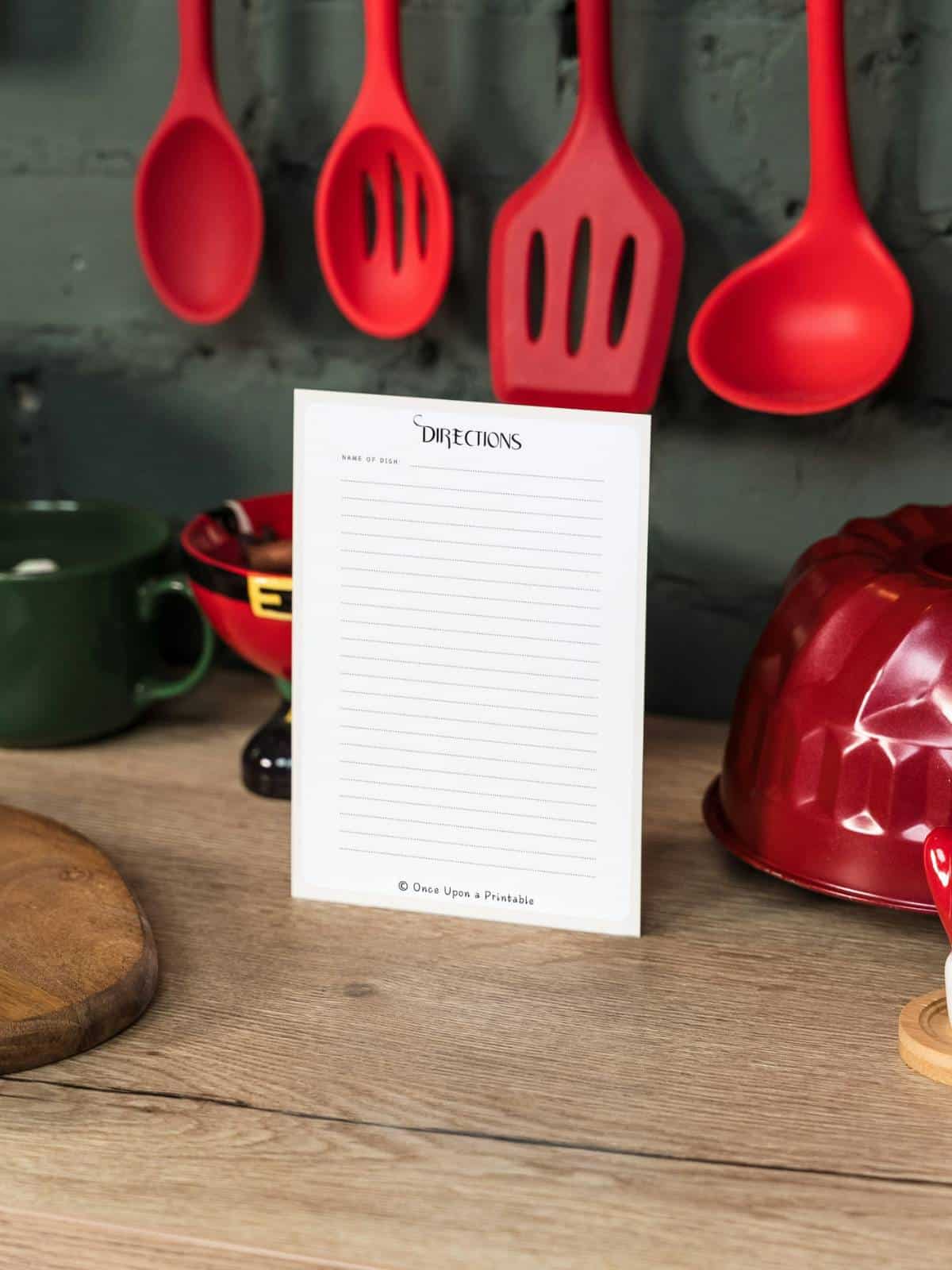Nutcracker-themed recipe card showing the backside with a space for "directions", sitting in front of red kitchen utensils on a countertop.