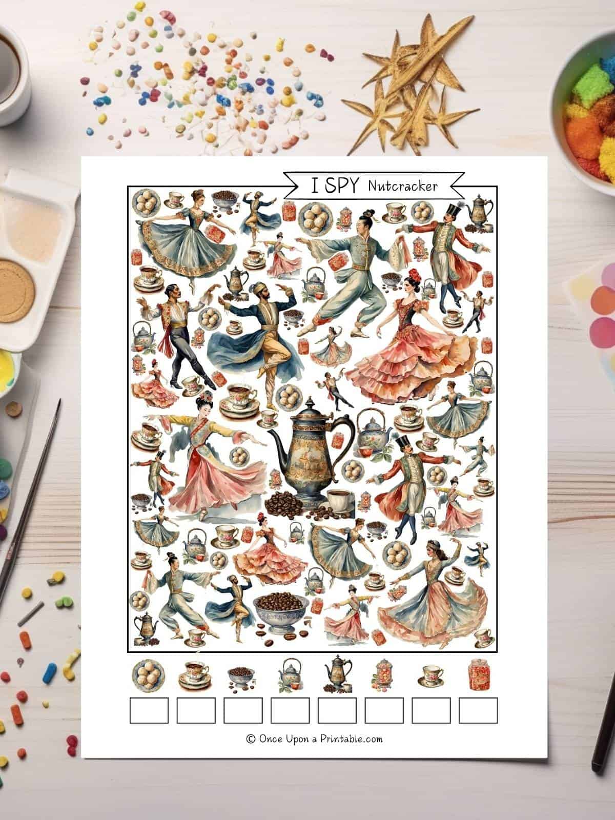 Nutcracker themed I spy printables with brightly colored watercolor graphics on a page sitting on a table with art supplies like glitter.