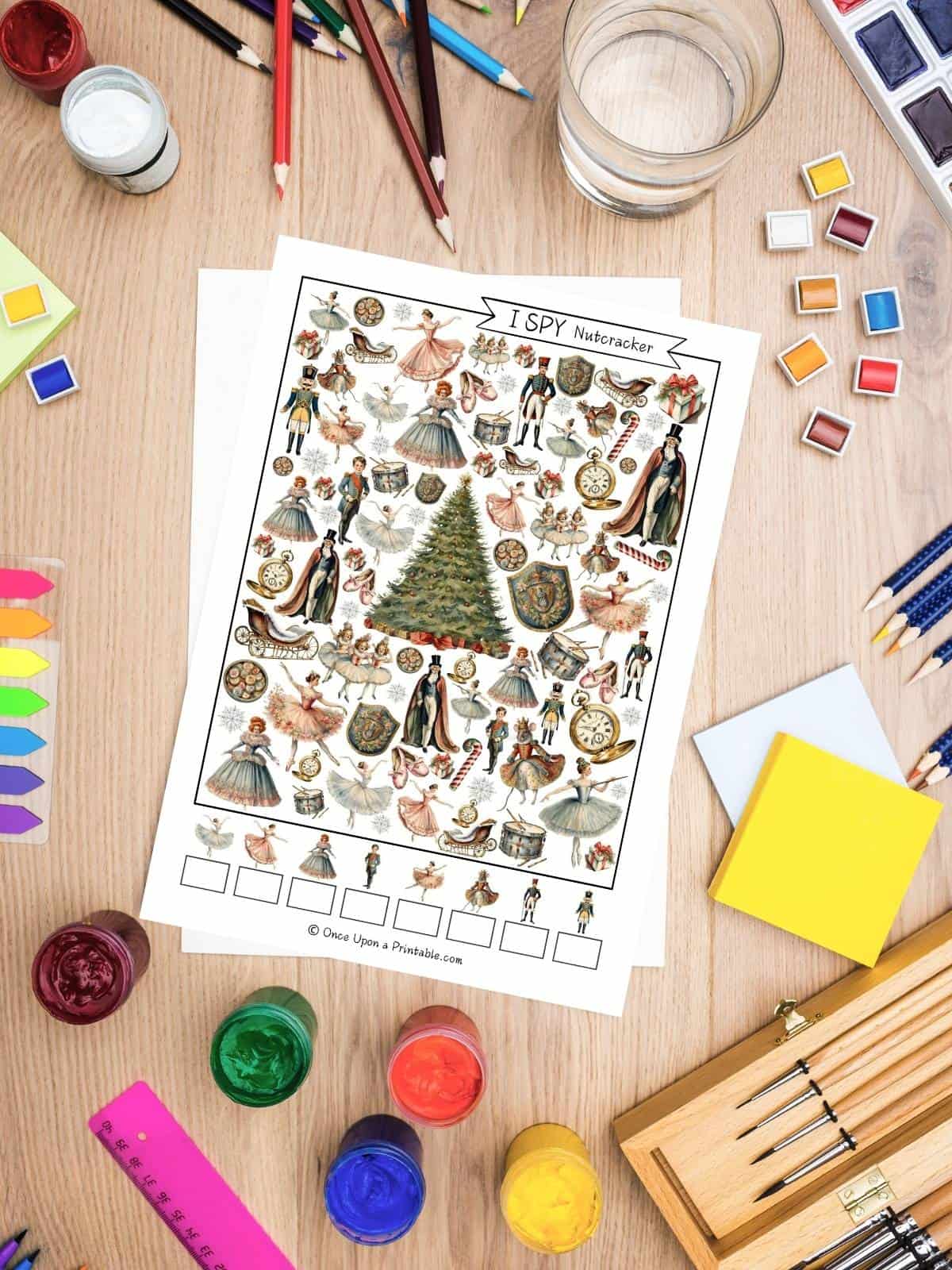 The Nutcracker themed I spy printables with brightly colored graphics sitting on a table with art supplies like crayons, paints, pencils, etc.