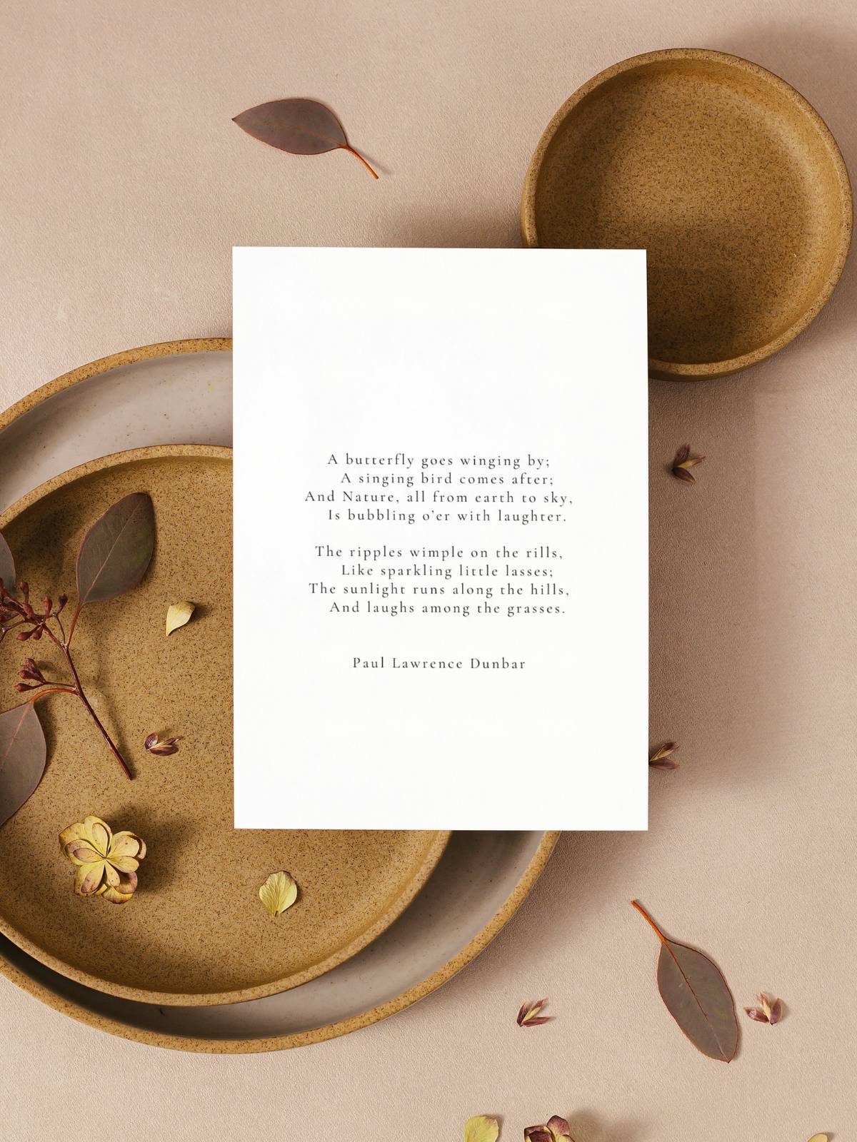 A fall greeting card with a poem by Paul Lawrence Dunbar printed on it, sitting on pottery plates with dried leaves.