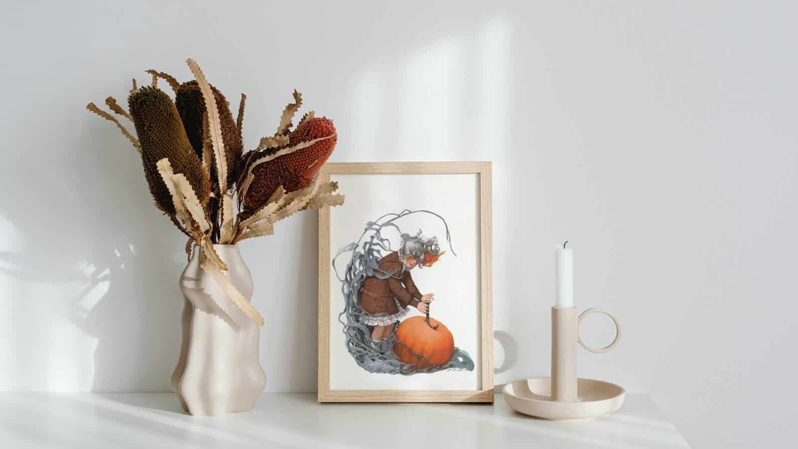 An illustration of a girl holding onto a large pumpkin, framed sitting next to a candle stick and a vase full of dried flowers.