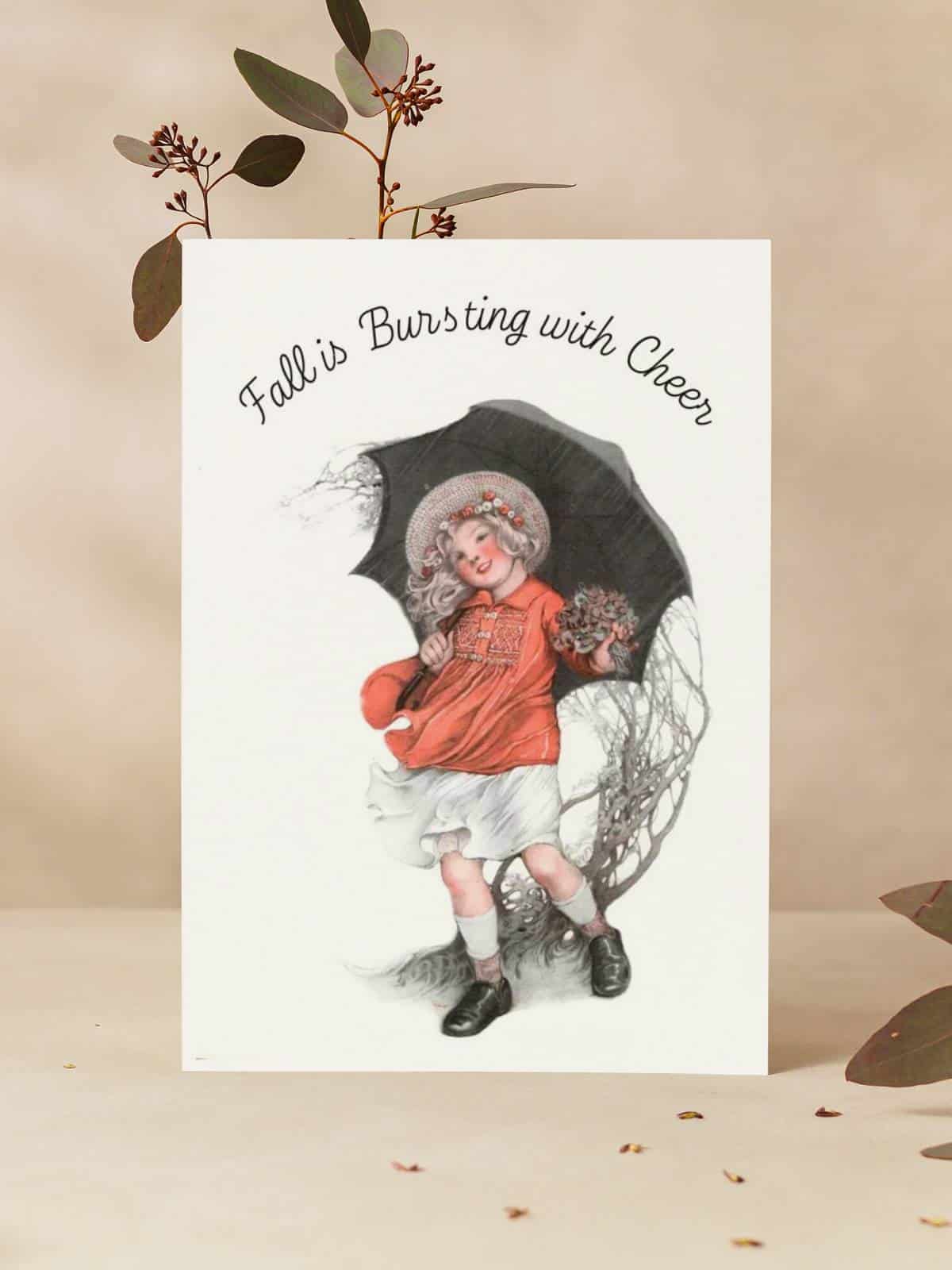 Girl with umbrella walking in the wind, illustrated by Sarah Stilwell-Weber a greeting card sitting on a vase with dried flowers.