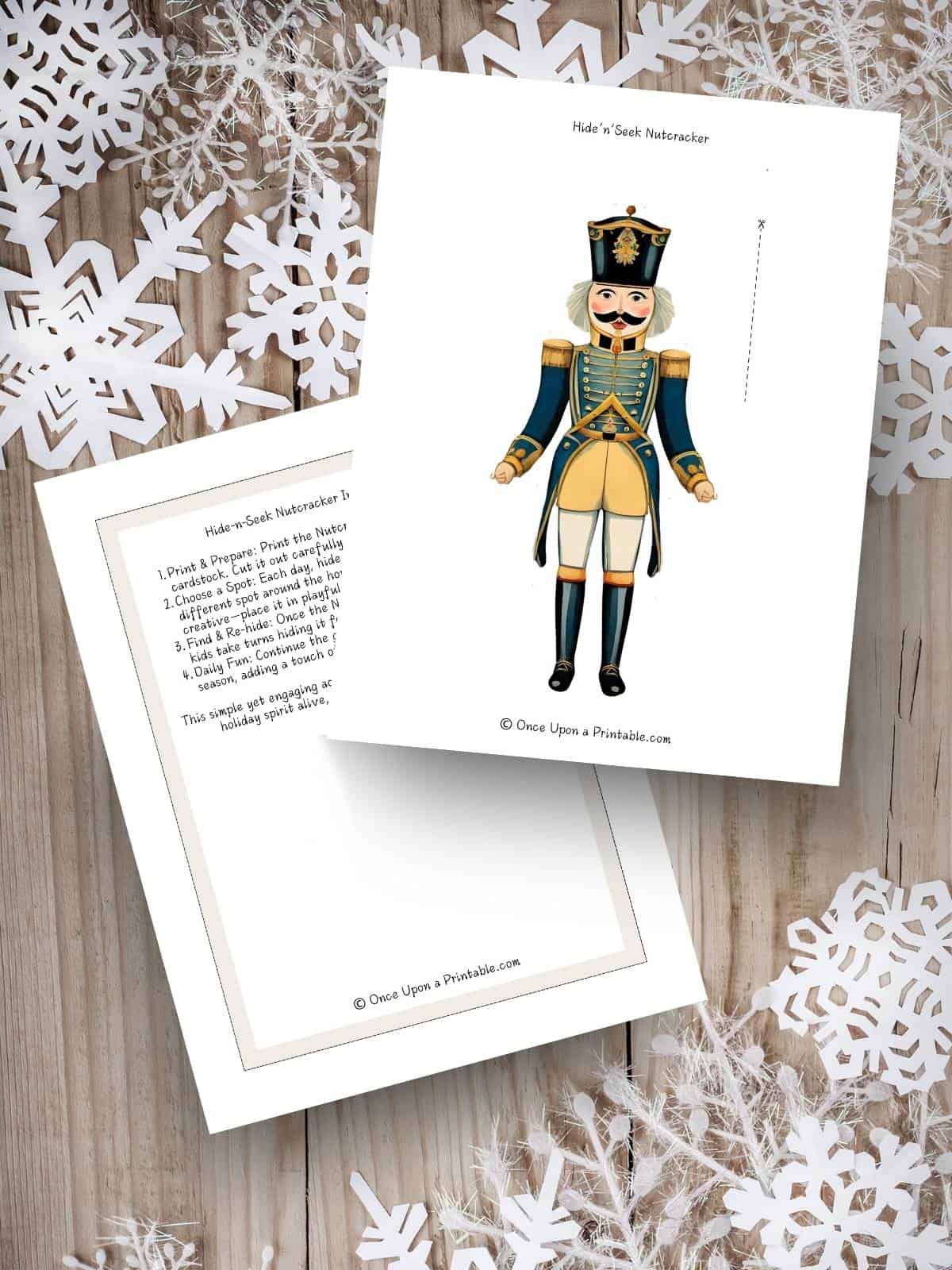 Nutcracker Hide and Seek printable paper doll to cut out and hide like Elf on the shelf displayed on a wooden table with paper white snowflakes.