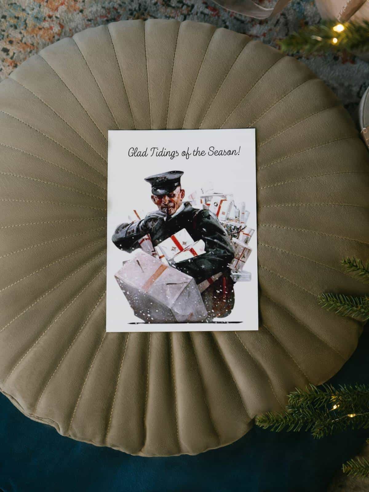Postal worker with an armful of packages delivering for Christmas, greeting card laying on a griege puff on the floor.