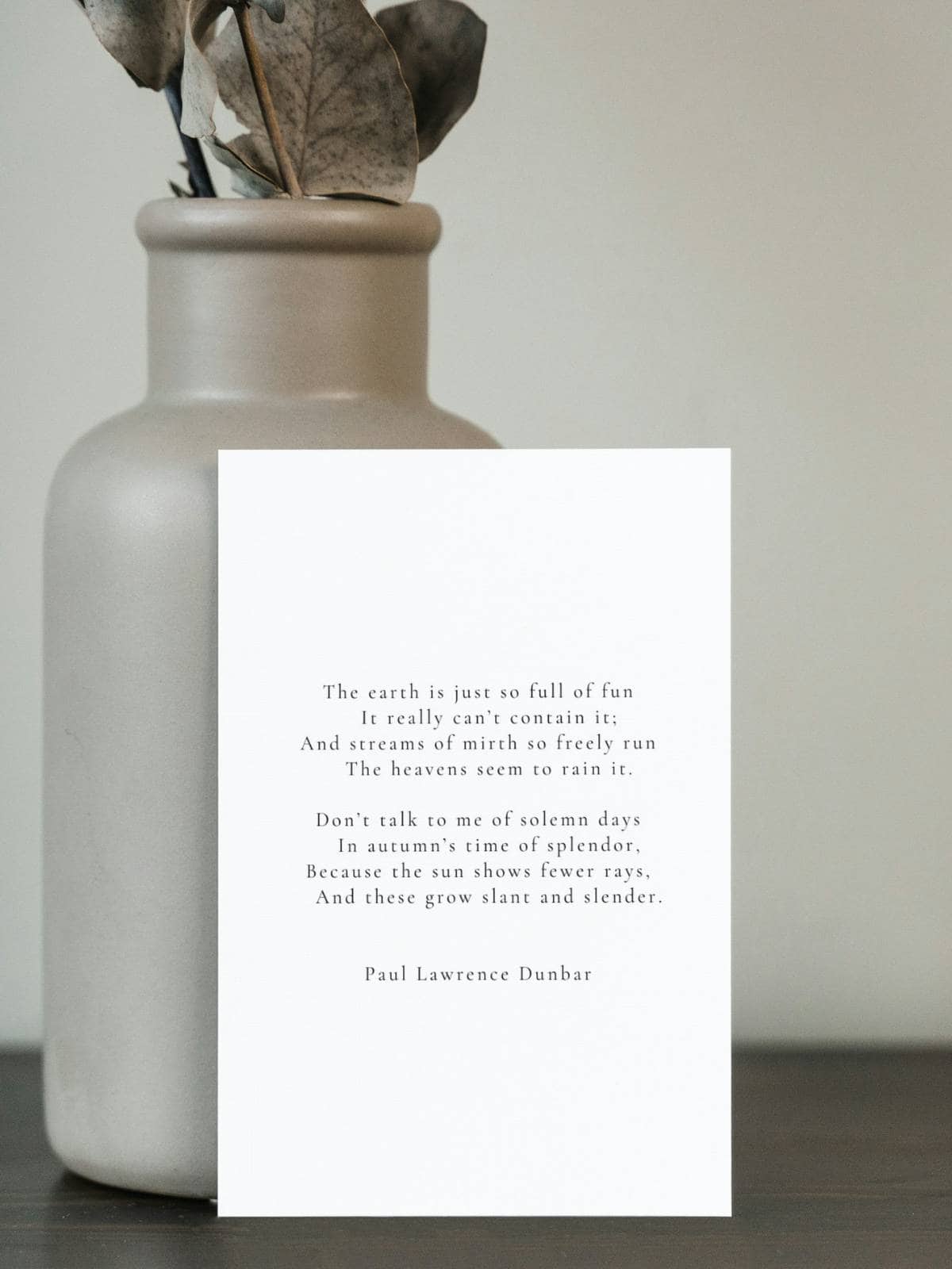 A poem by Paul Lawrence Dunbar on a greeting card standing up on a pottery vase. 