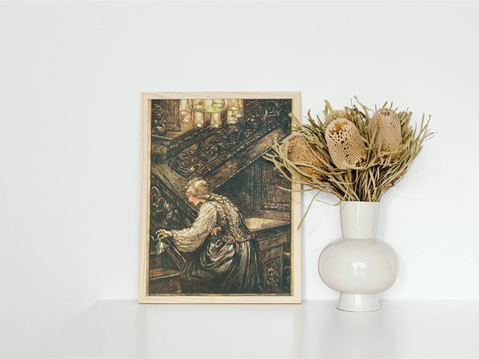 Brother's grimm illustration by Arthur Rackham of the Frog Prince, framed and displayed next to a vase of dried flowers.