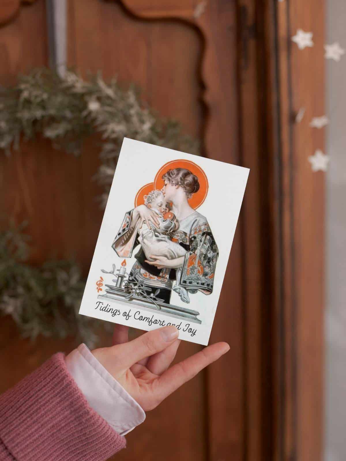 Vintage illustrated Christmas card with a mother carrying her sleeping child being held in the hand of a woman in front of a wooden door with a christmas tree wreath.