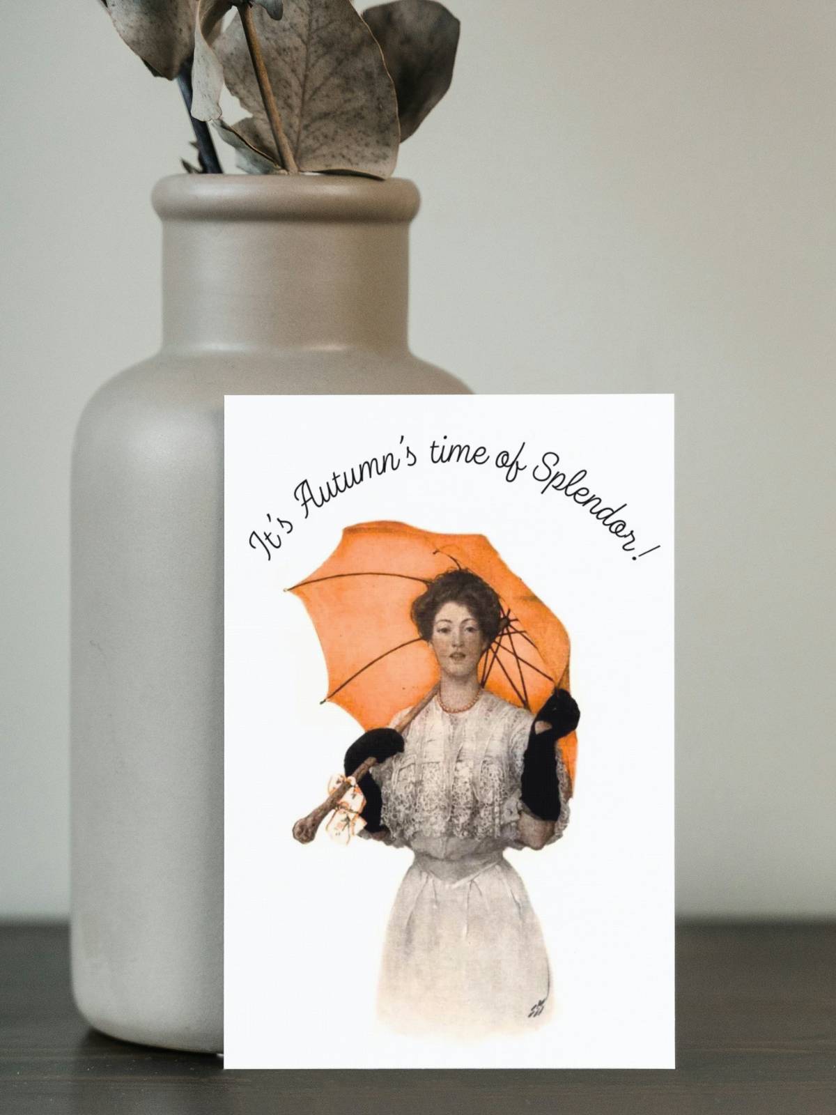 A woman holding a red umbrella, illustrated by Sarah Stilwell-Weber, on a greeting card standing up on a pottery vase. 