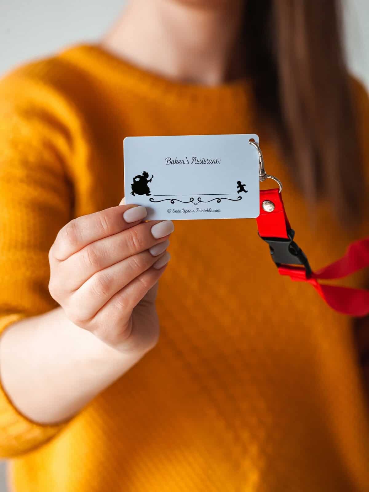 "Baker's Assistant" Gingerbread man illustrated name tag being held up by a woman.