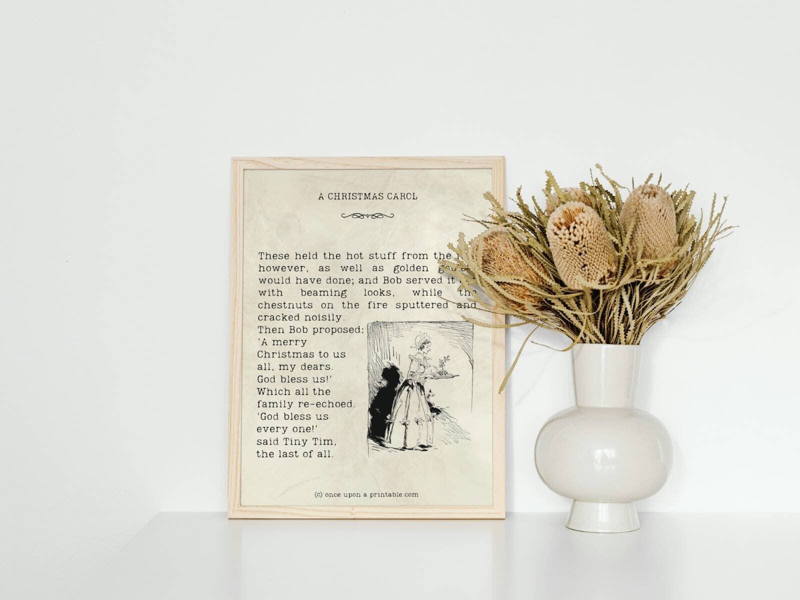 A Christmas Carol quotes framed with a vase and dried flowers next to it.
