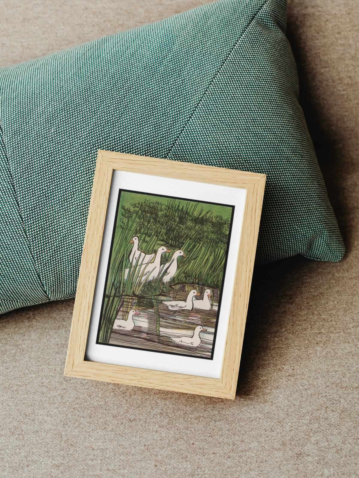 Vintage illustration of ducks in a stream framed and sitting on a green pillow.