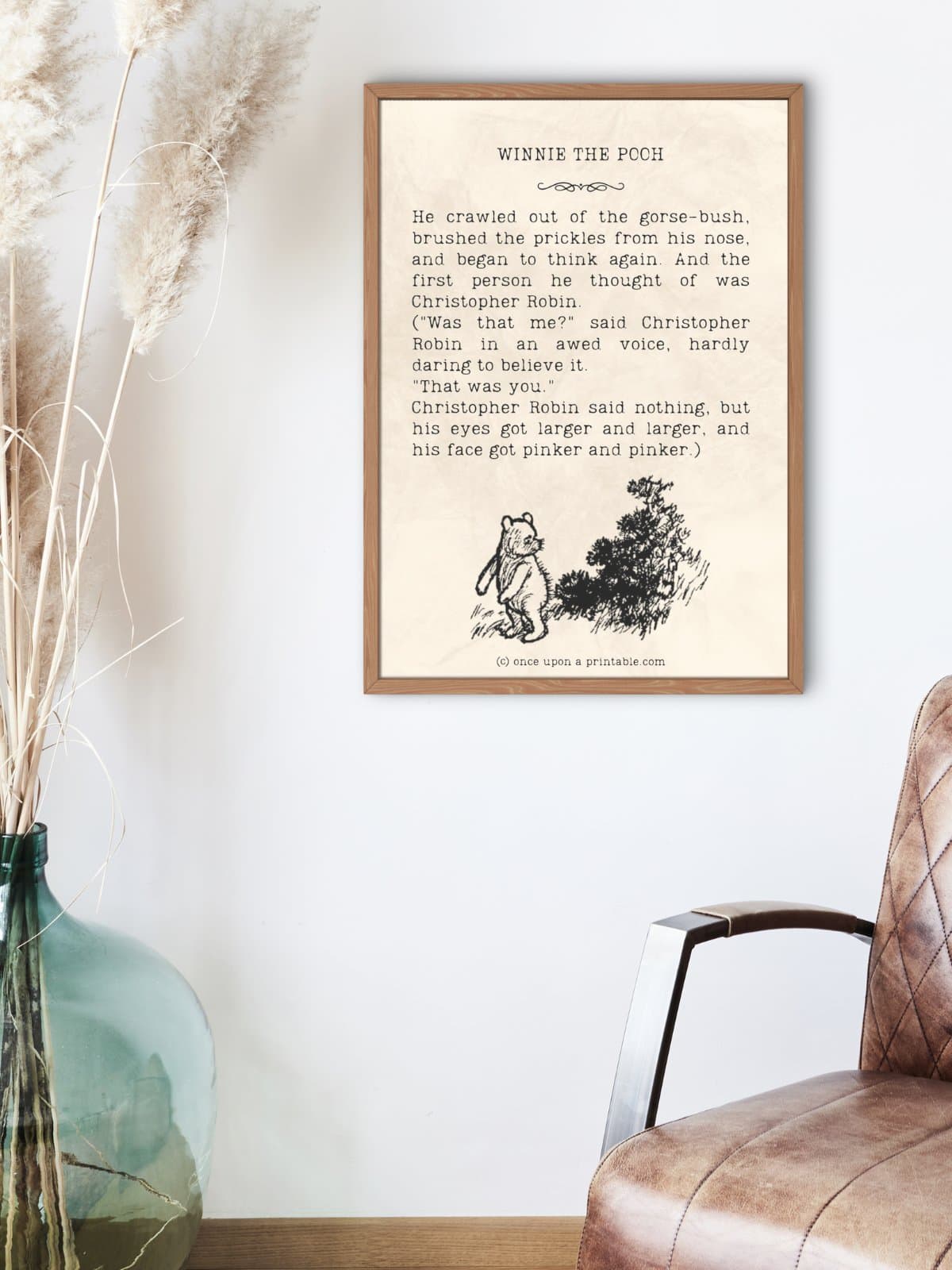 Framed Winnie the Pooh quote with an original illustration by E. H. shepard in black and white displayed above a leather chair and next to a blue glass vase of pampas grass.