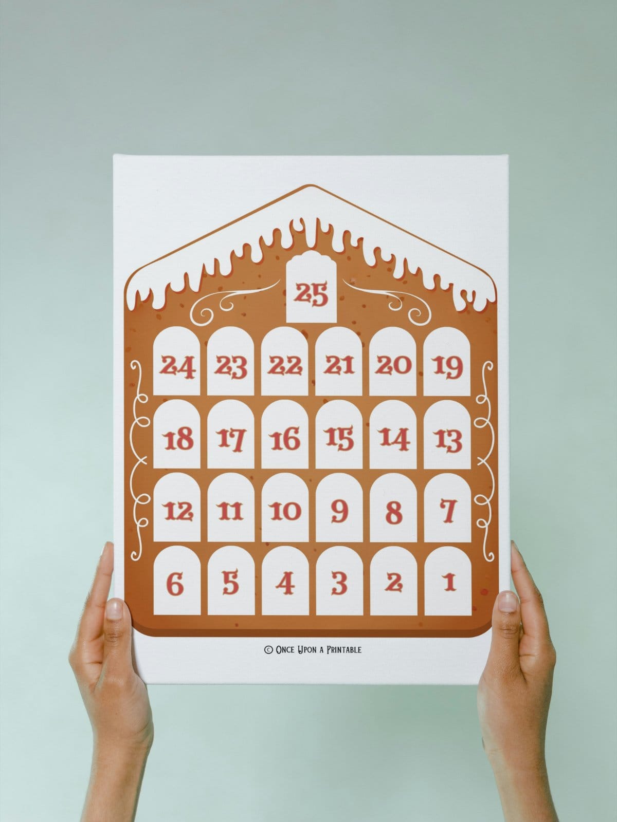 The bright and colorful graphic of a Gingerbread house countdown calendar for christmas being held in a woman's hands.