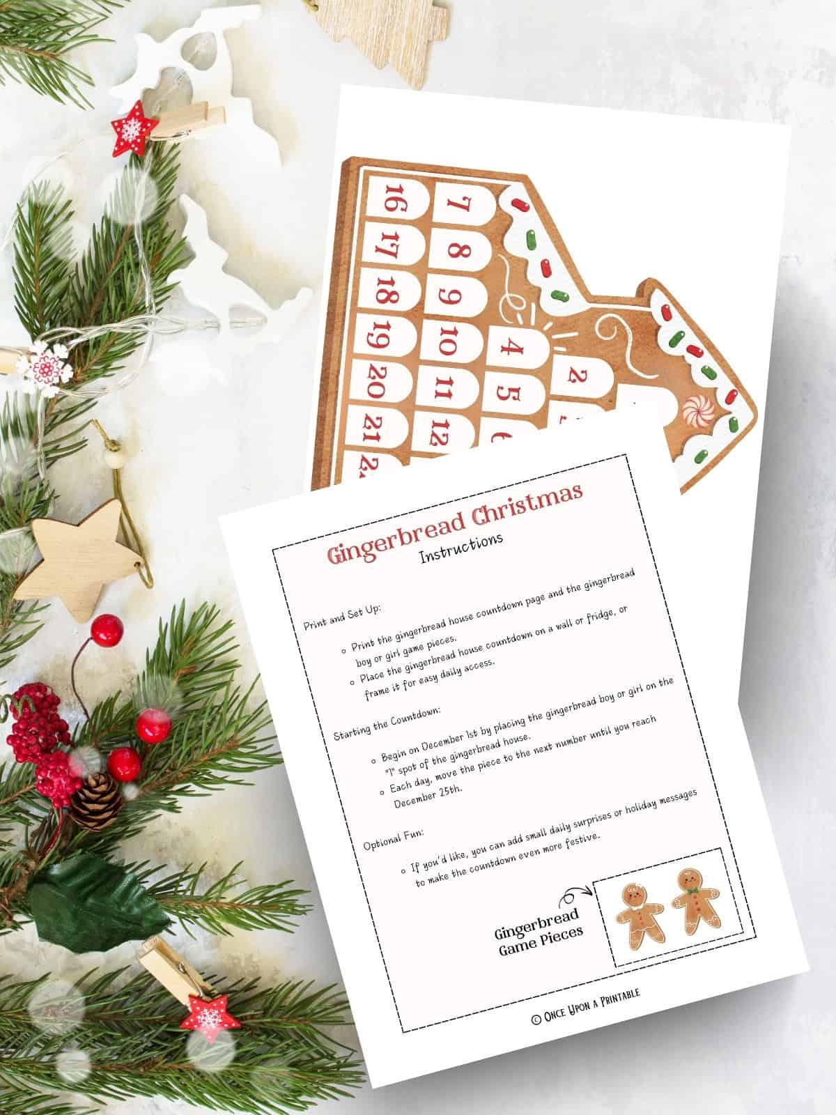 Gingerbread house Christmas countdown calendar pages printed and laying on a white table with garland and Christmas ornaments.
