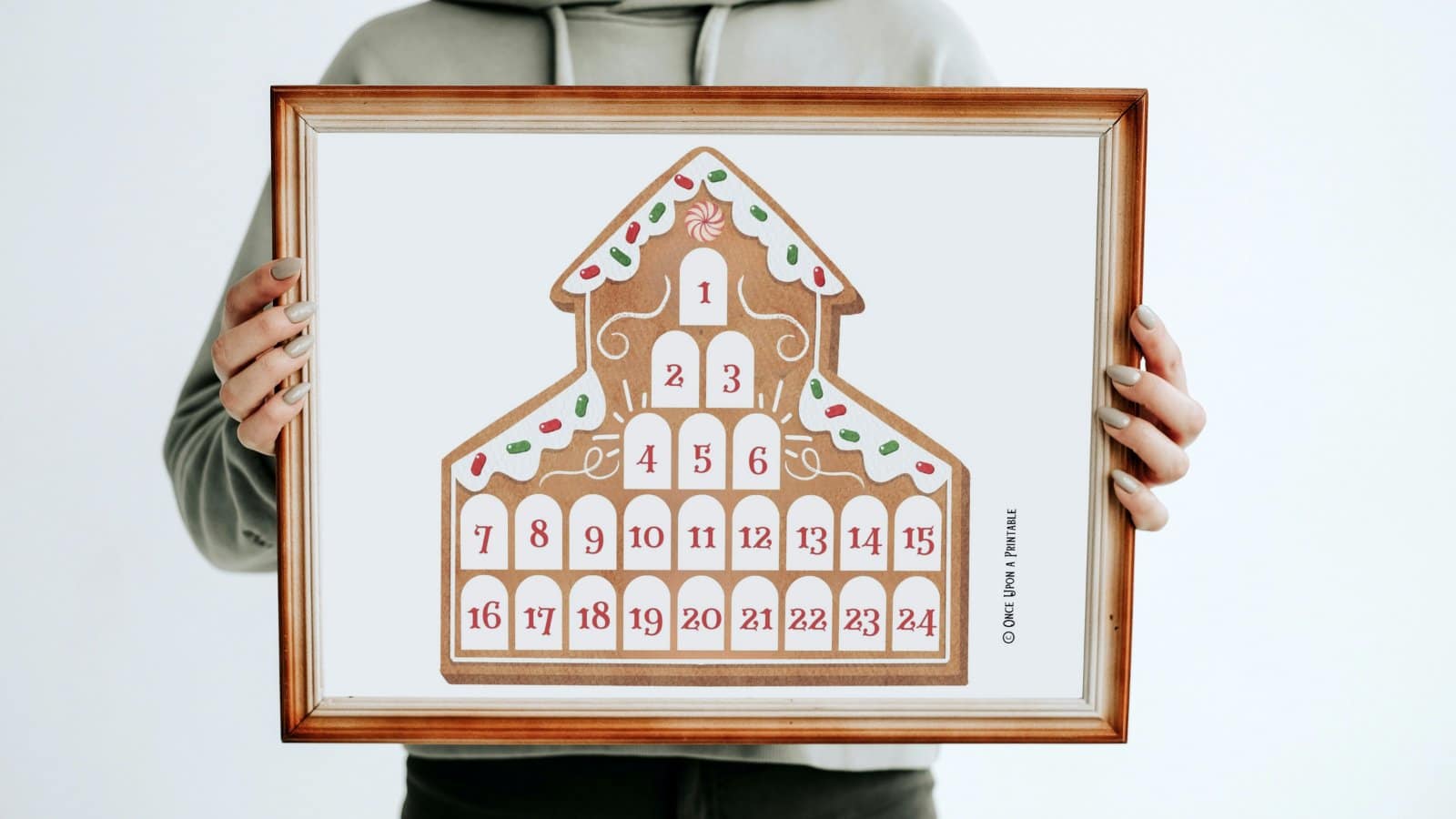 Gingerbread house countdown calendar framed and held in the hands of a woman.