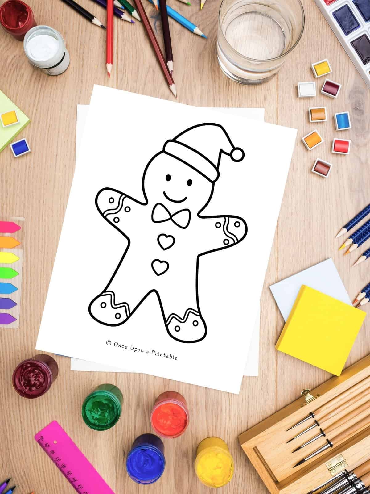 A gingerbread man santa claus coloring pages sitting next to coloring supplies like paints, pencils, etc.