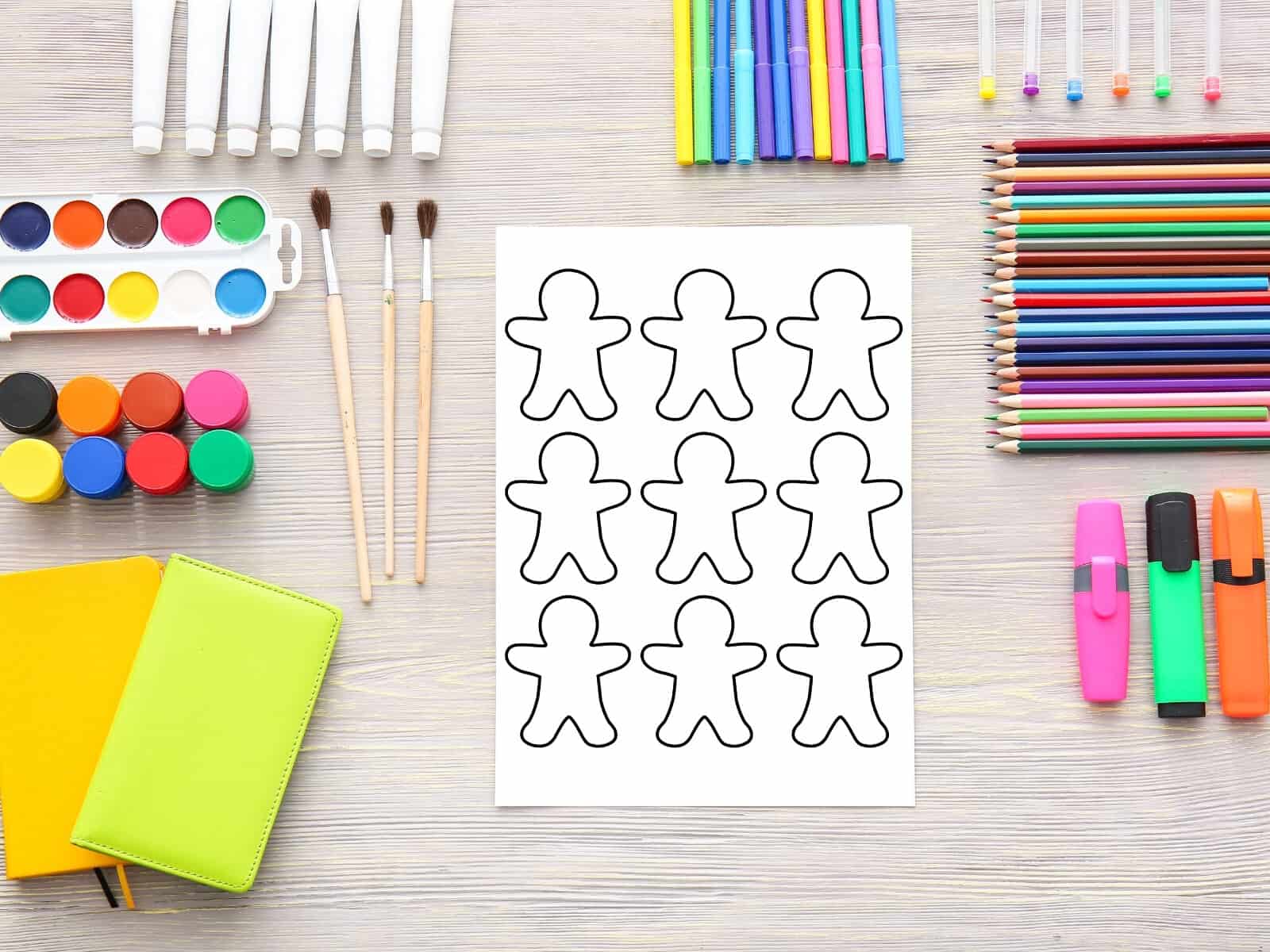 Gingerbread person template printable sitting next to all kinds of coloring supplies like pencils, markers, paints, etc.