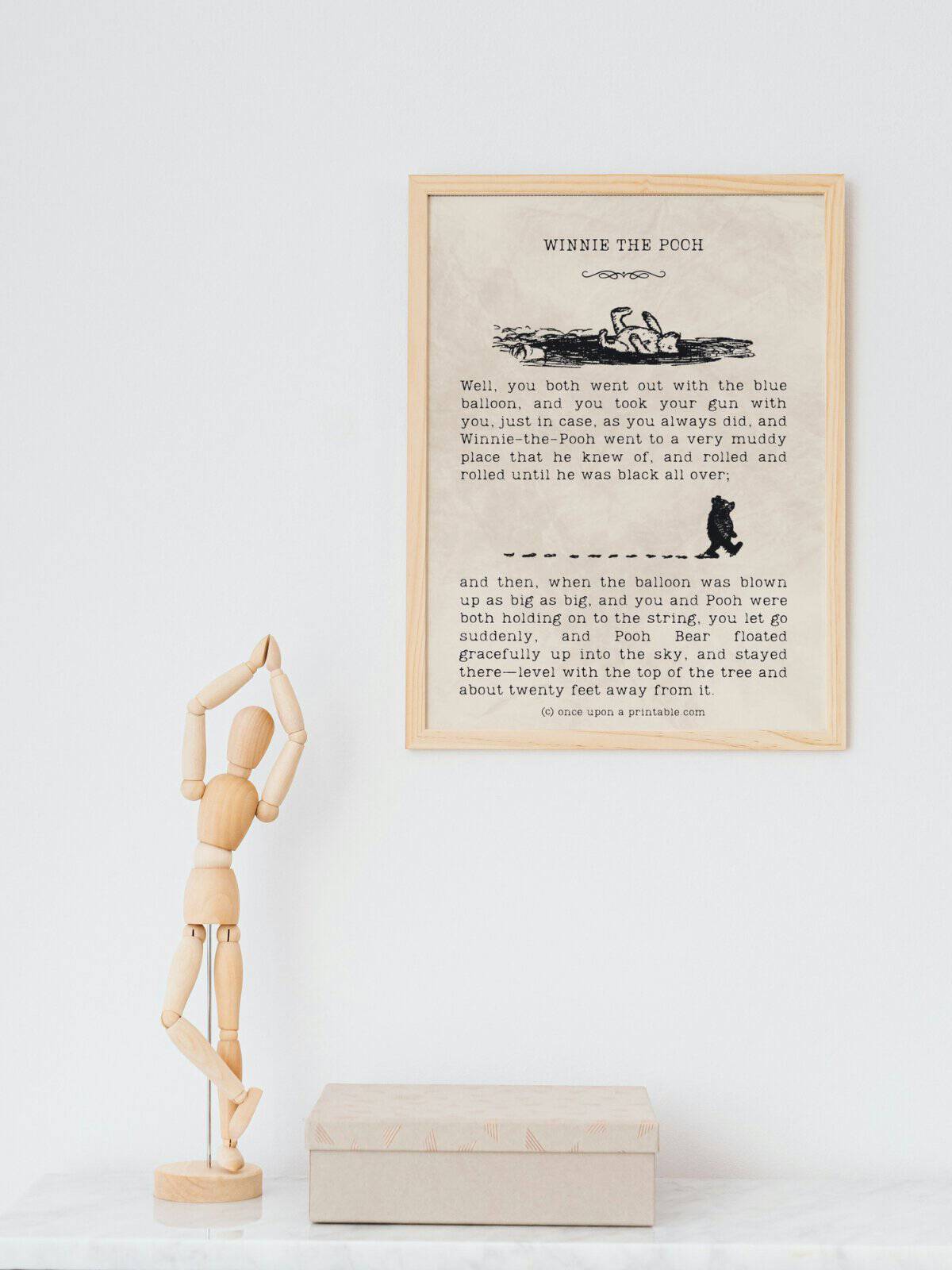 Illustrated quotes from the book Winnie the Pooh framed and displayed above a wooden drawing doll and a book.