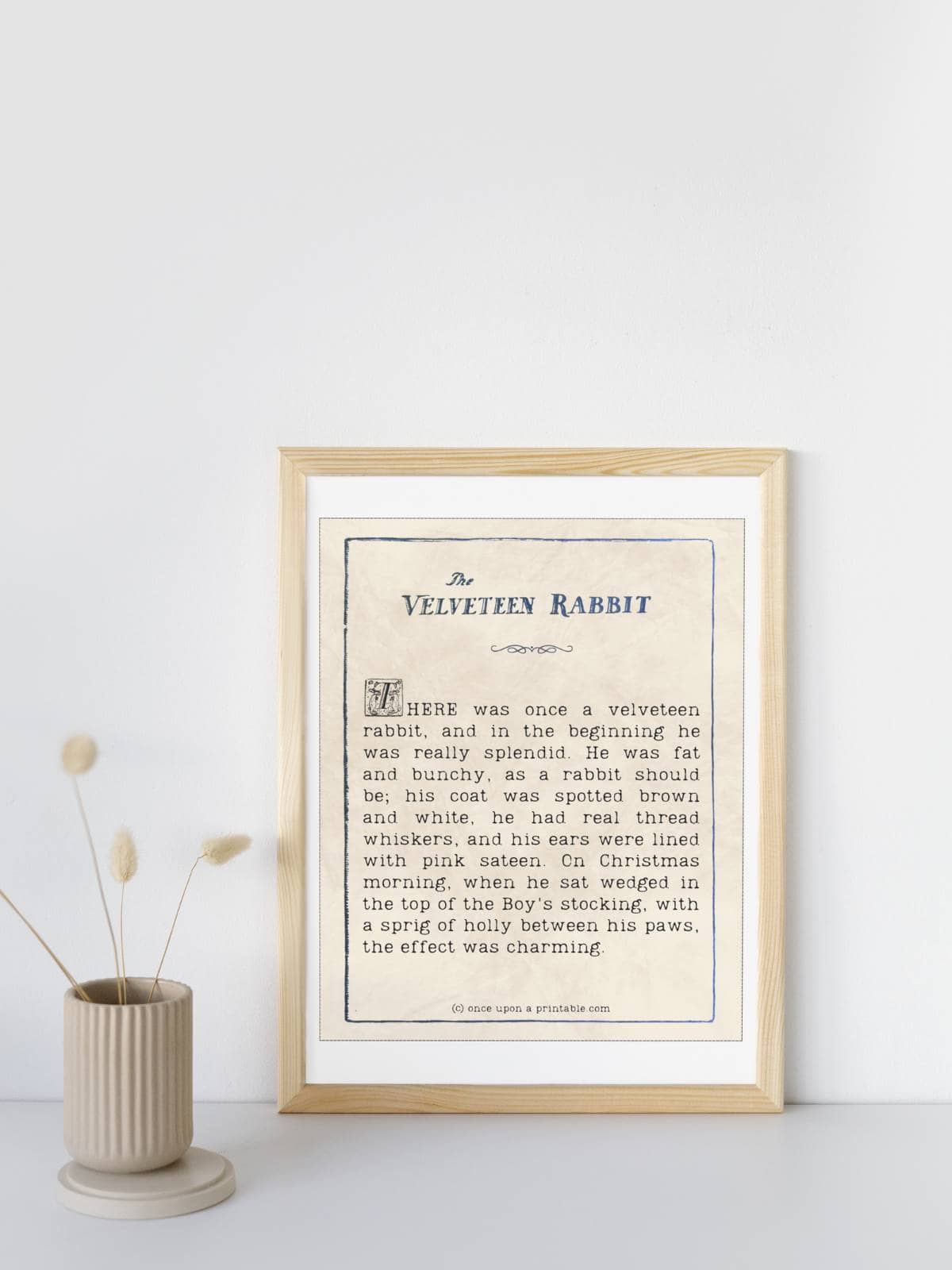A quote from the book The Velveteen Rabbit framed and displayed next to a vase with one dried flower in it.