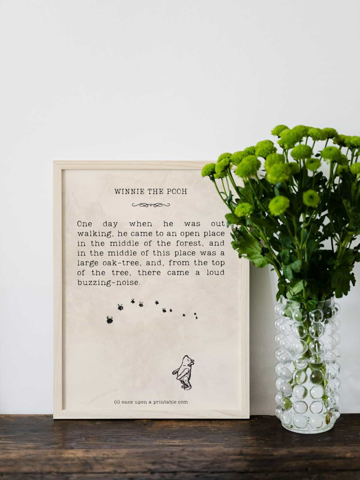 Winnie the Pooh quotes and illustrations framed as decor next to a vase full of green sprigs. 