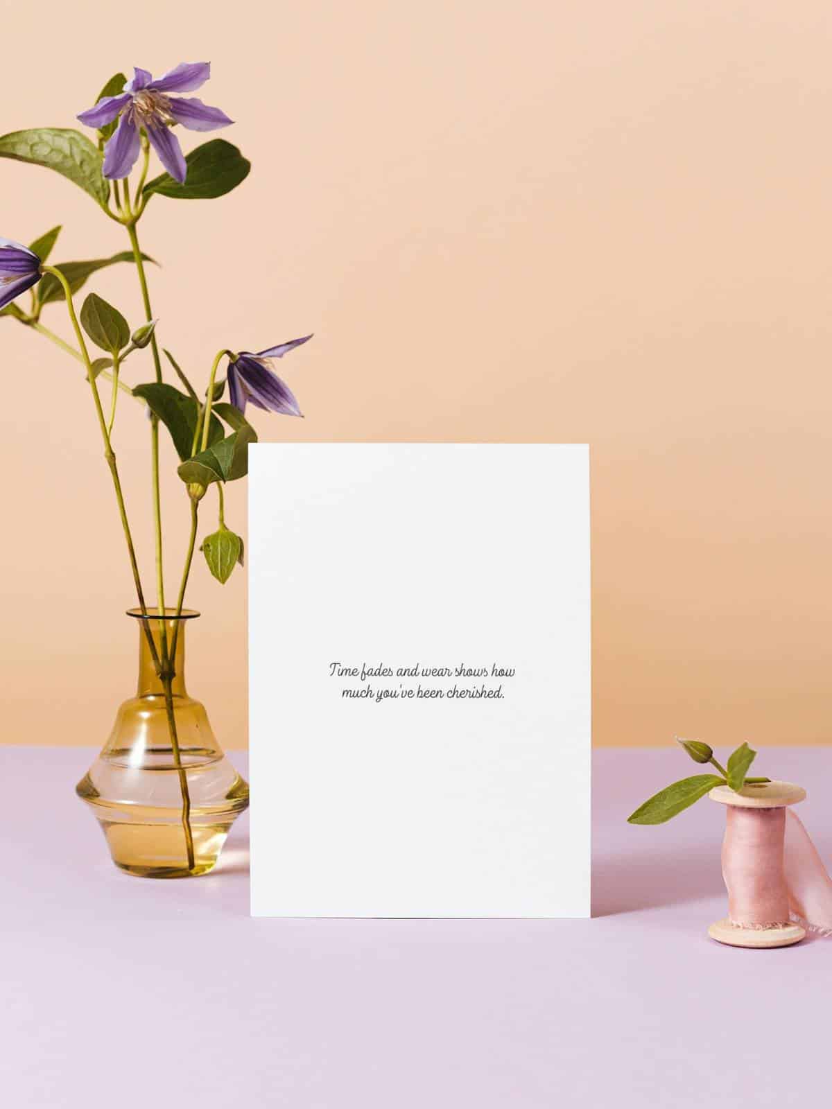 A note card sentiment layed with a vase and flowers and a spindle of ribbon.
