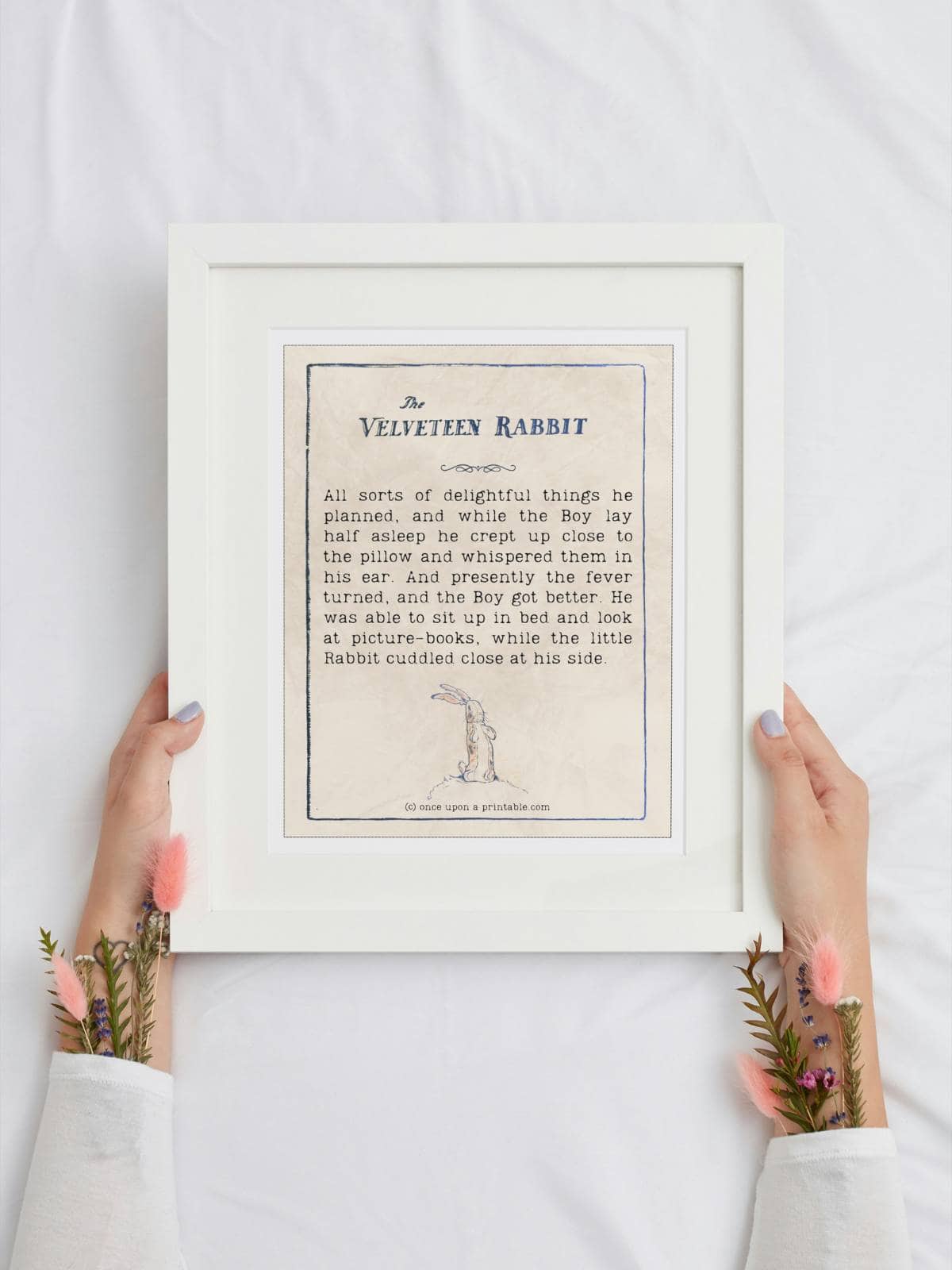 A Velveteen Rabbit quote framed and held by two female arms with flowers sticking out of her sleeves.