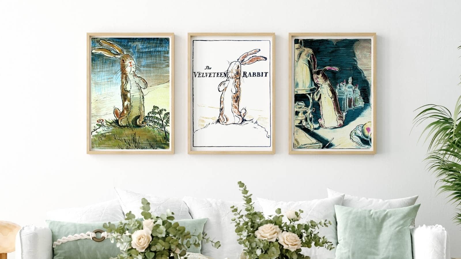 Three framed vintage illustrations of the Velveteen Rabbit displayed on a living room wall above light colored furniture and a fancy flower arrangement.