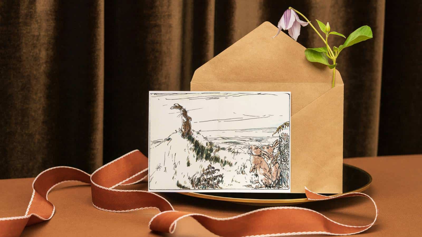 The Velveteen Rabbit note card and envelope sitting on a plate by an orange velvet ribbon.