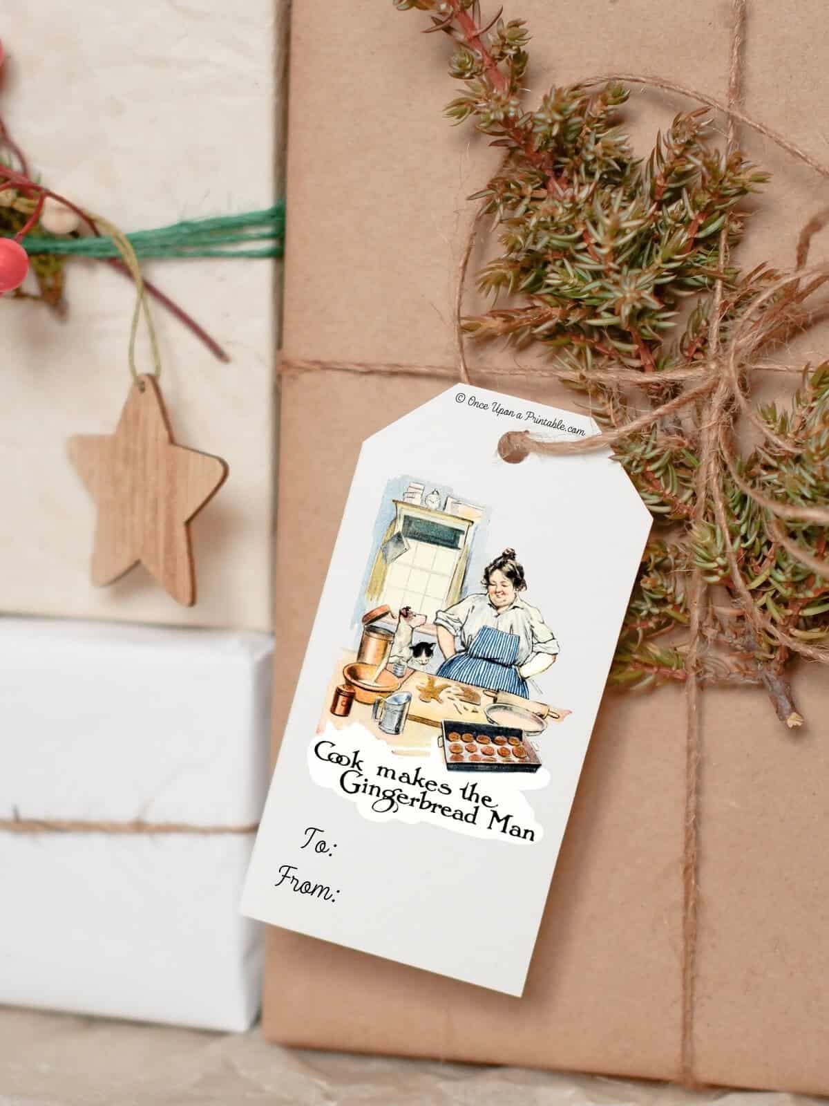A vintage illustration from the book The Little Gingerbread Man on a gift tag tied to a brown paper package with twine and a sprig of evergreen.
