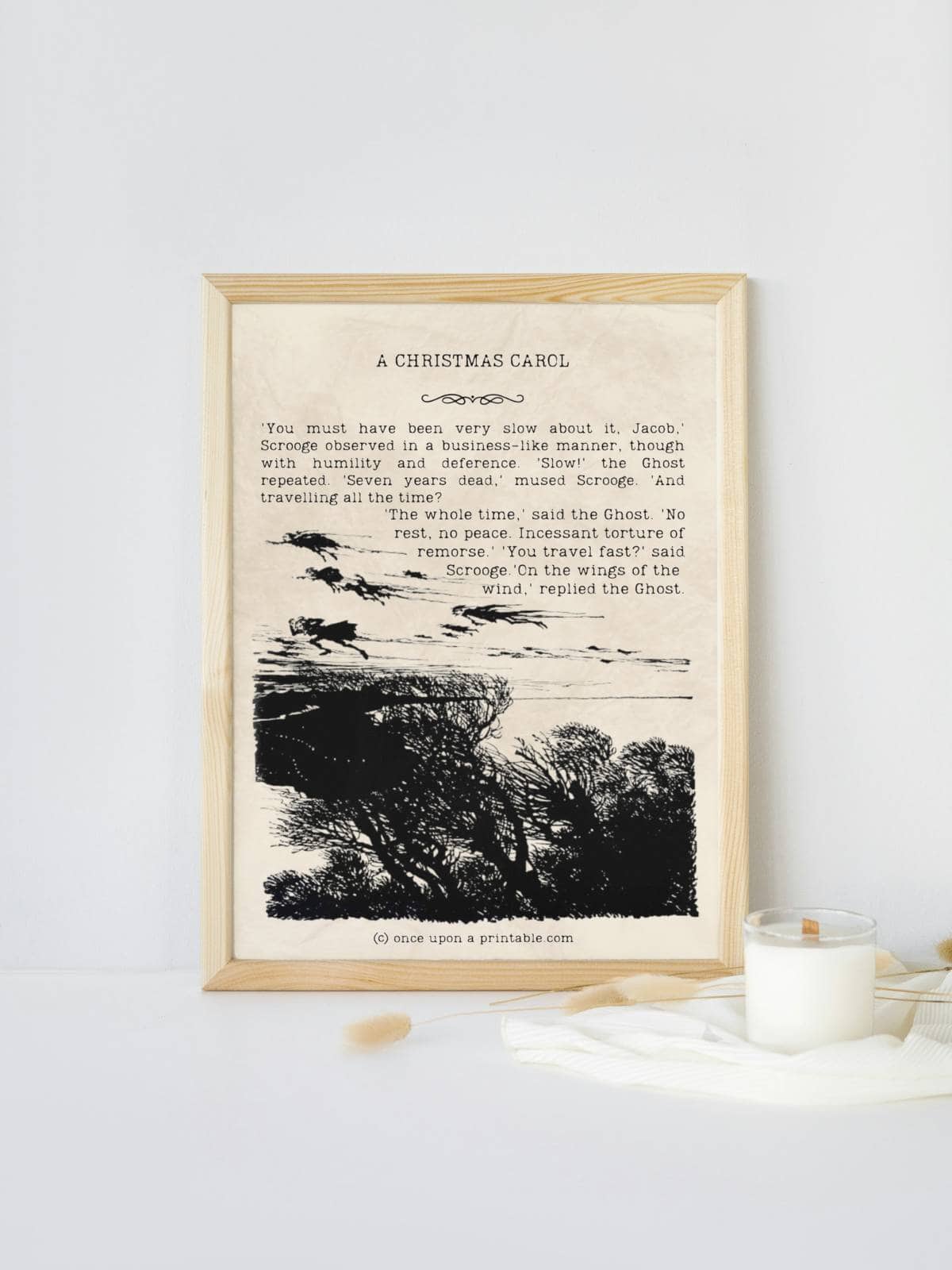 A Christmas Carol with original illustrations by Arthur Rackham framed and displayed next to a candle. 