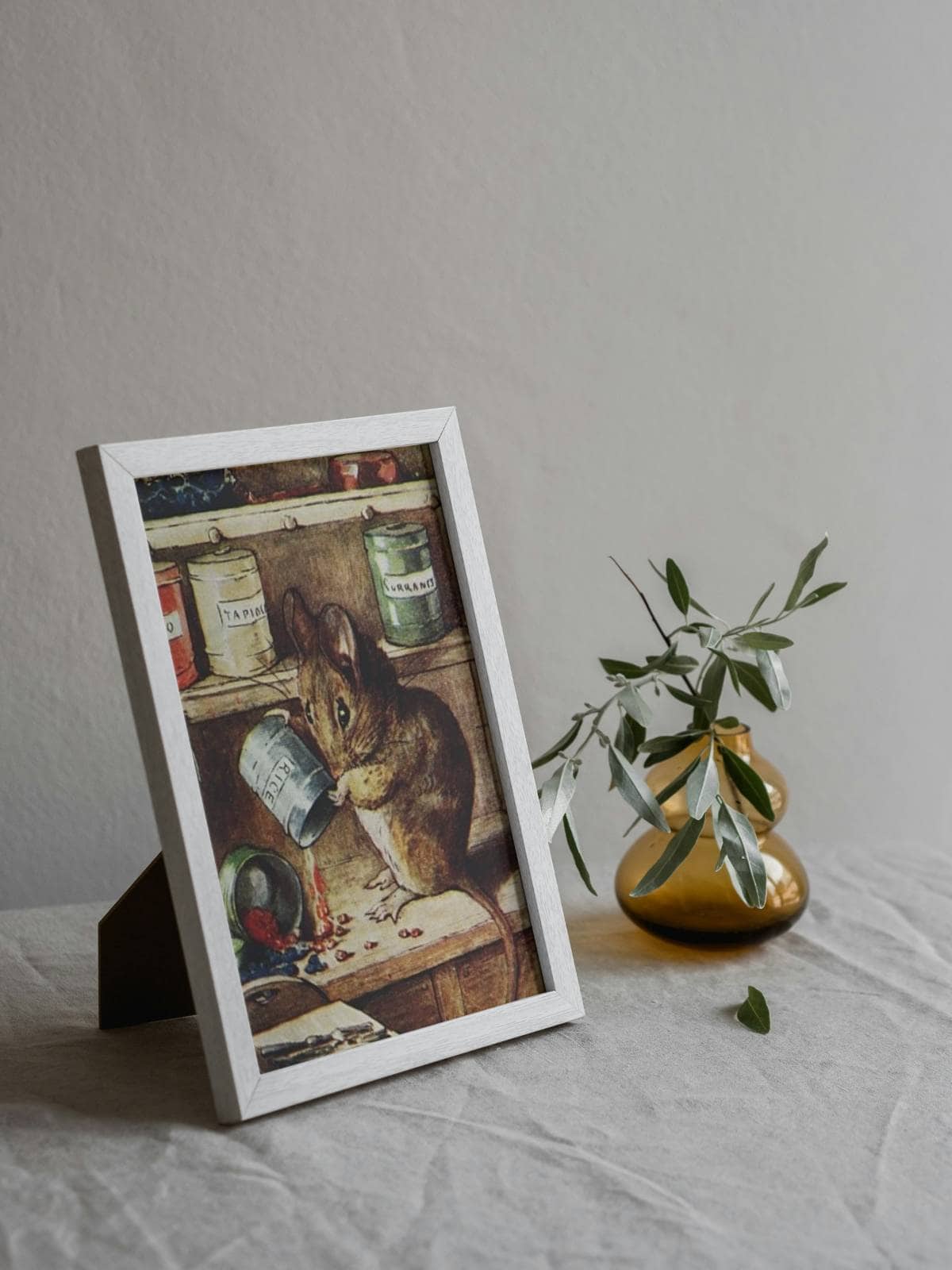 Beatrix Potter's "tale of two bad mice" illustration framed and displayed next to a bud case with a few sprigs.