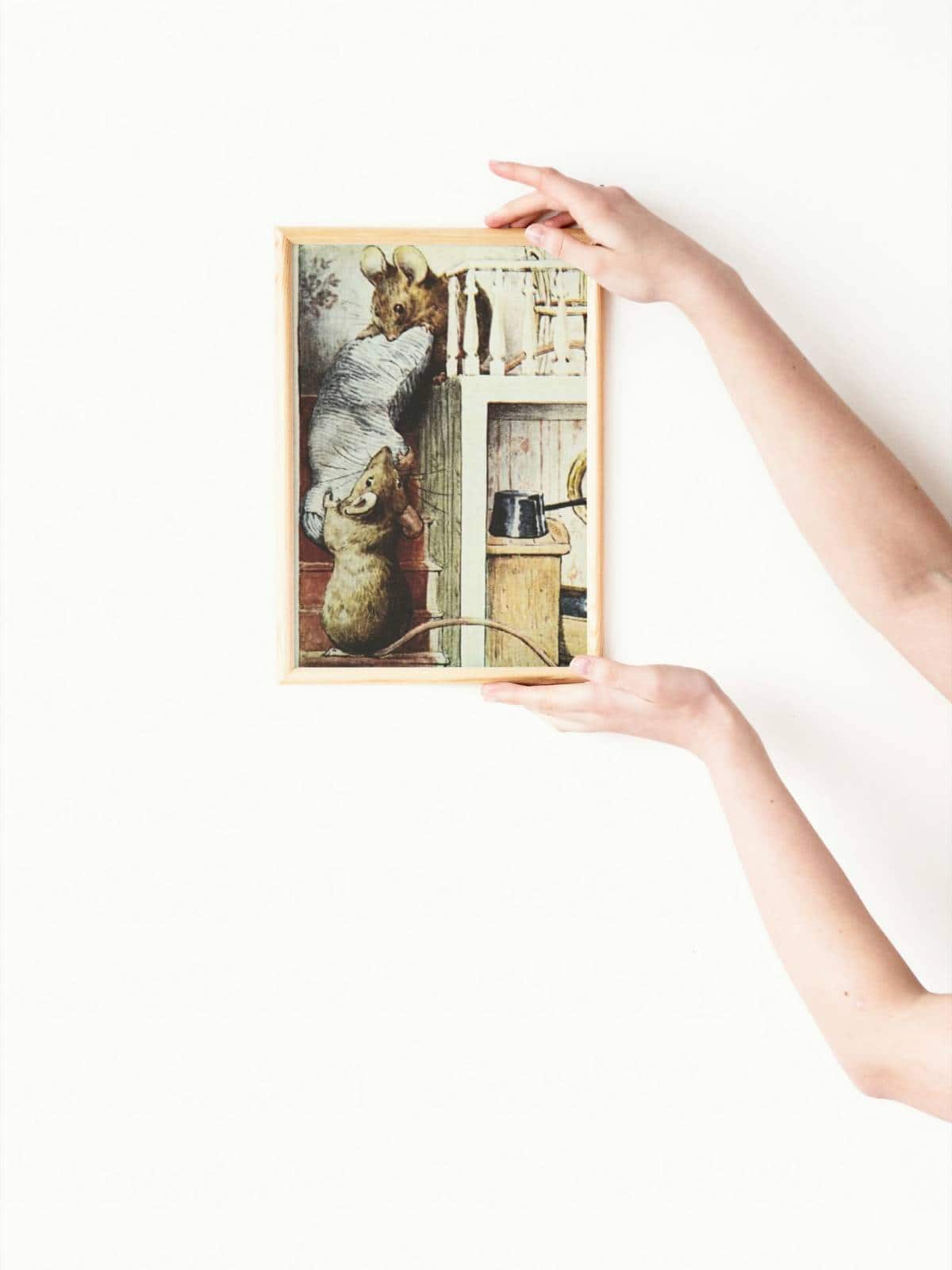 The tale of two bad mice illustration framed and held up by two female hands.