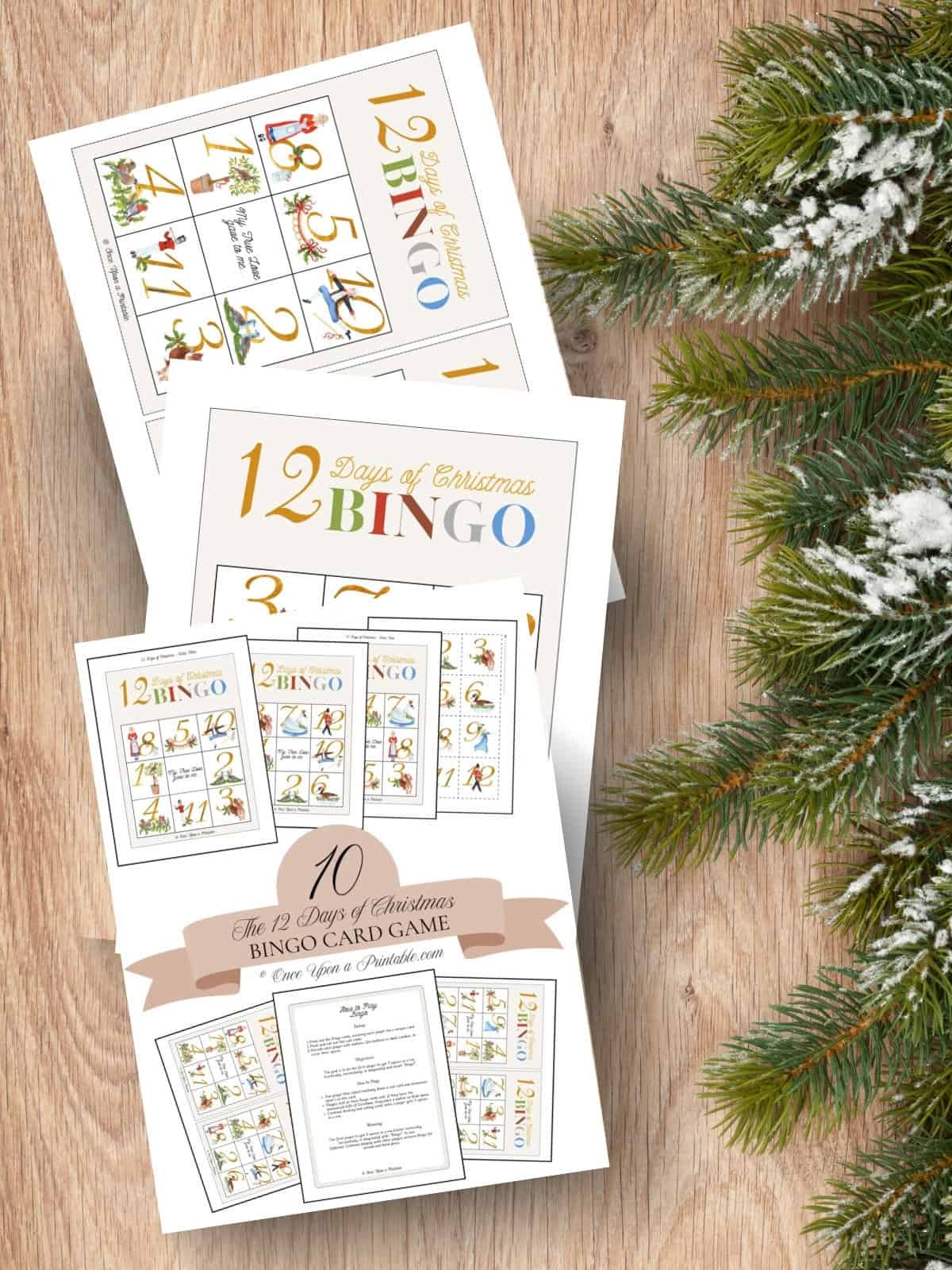 12 Days of Christmas Bingo cards, cover page, full page bingo card, and the mini version laying on a wooden surface with Christmas garland.