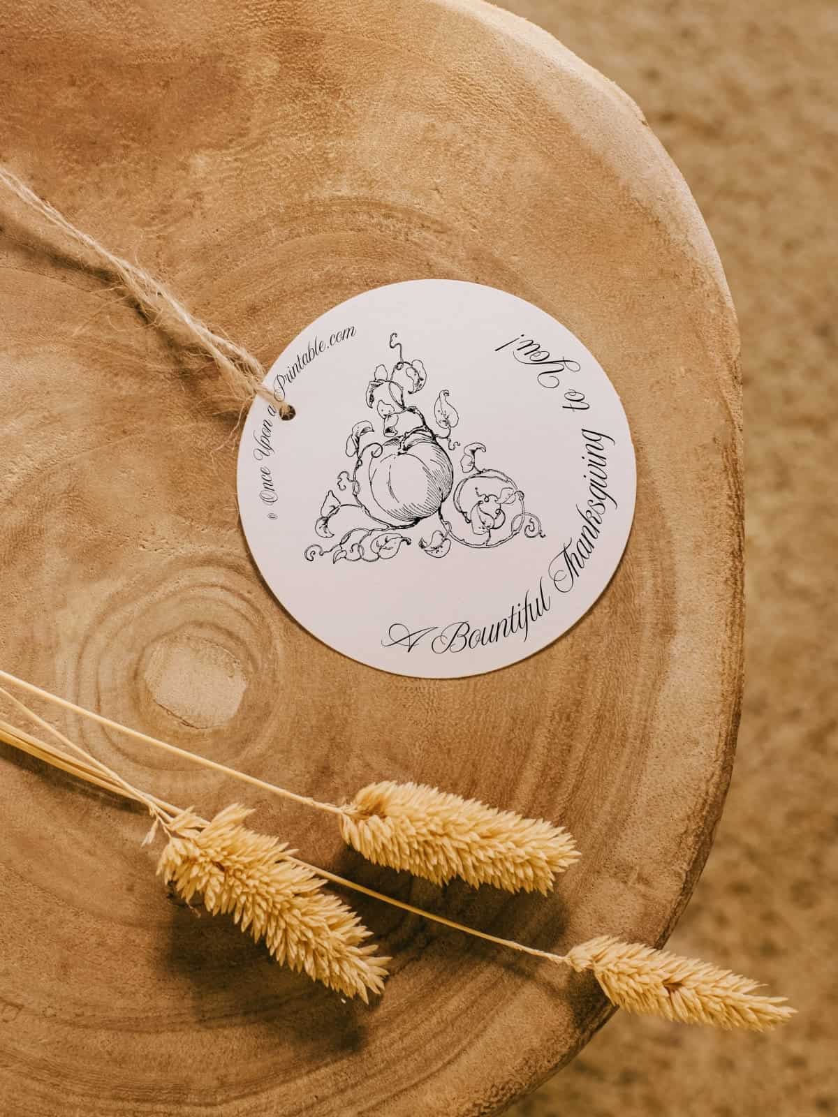 A circular thanksgiving tag with a vintage pumpkin illustration sitting on a wooden block with wheat.