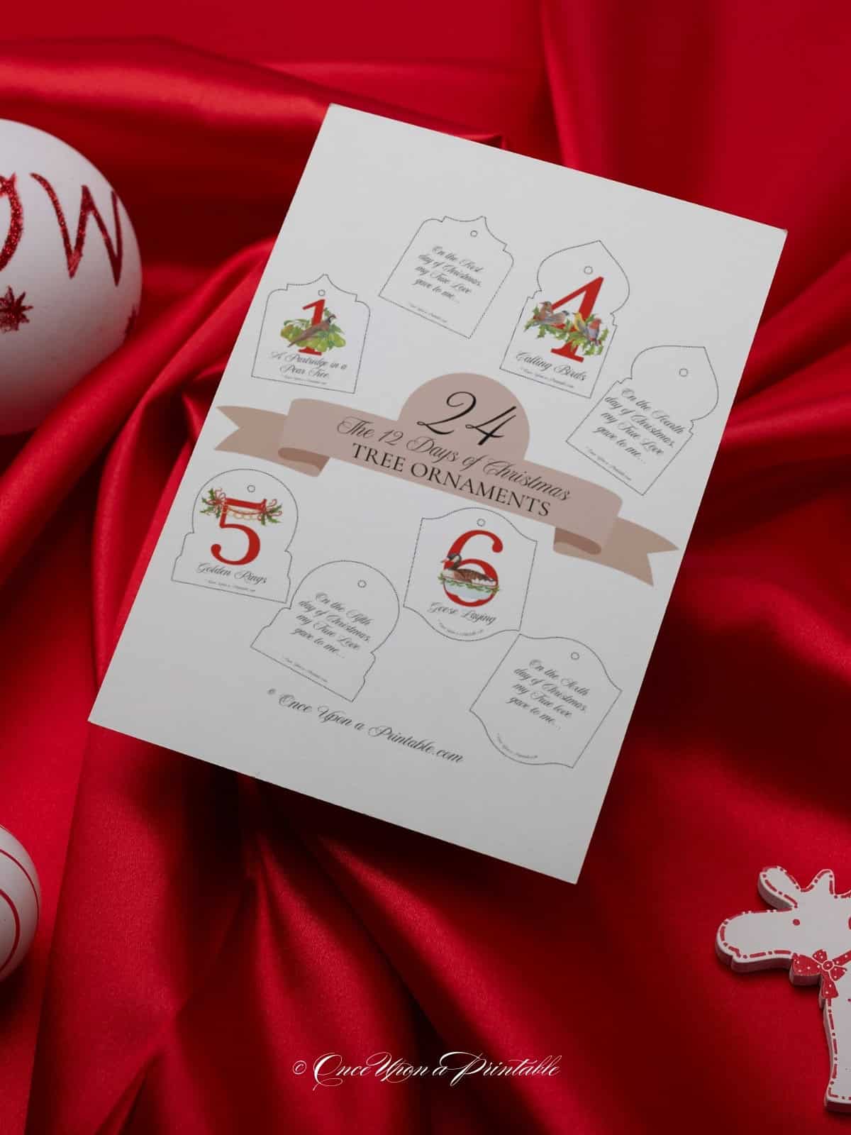 Bright and bold graphic christmas tree ornaments of the 12 days of Christmas printed and sitting on a sily bright red fabric.