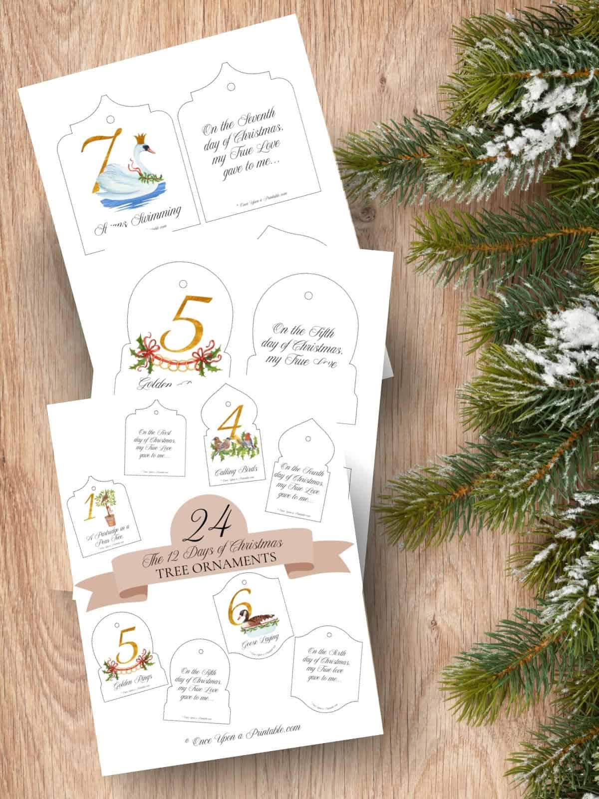 Soft and classic watercolor graphics of the 12 days of christmas tree ornaments printed and displayed on a wooden background with Christmas garland.