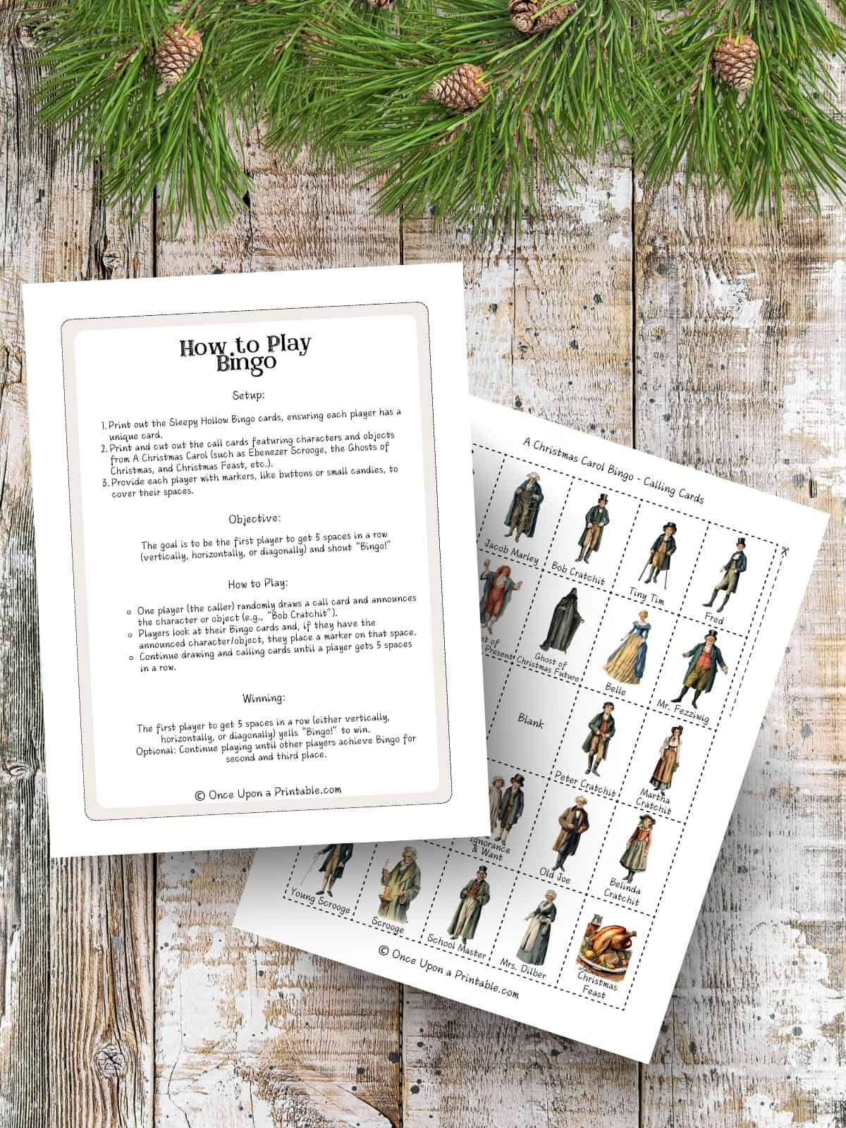 The instructions on how to play bingo as well as an example of a Christmas carol bingo card with original watercolor graphics of the book characters printed and sitting on a wooden surface with green garland.