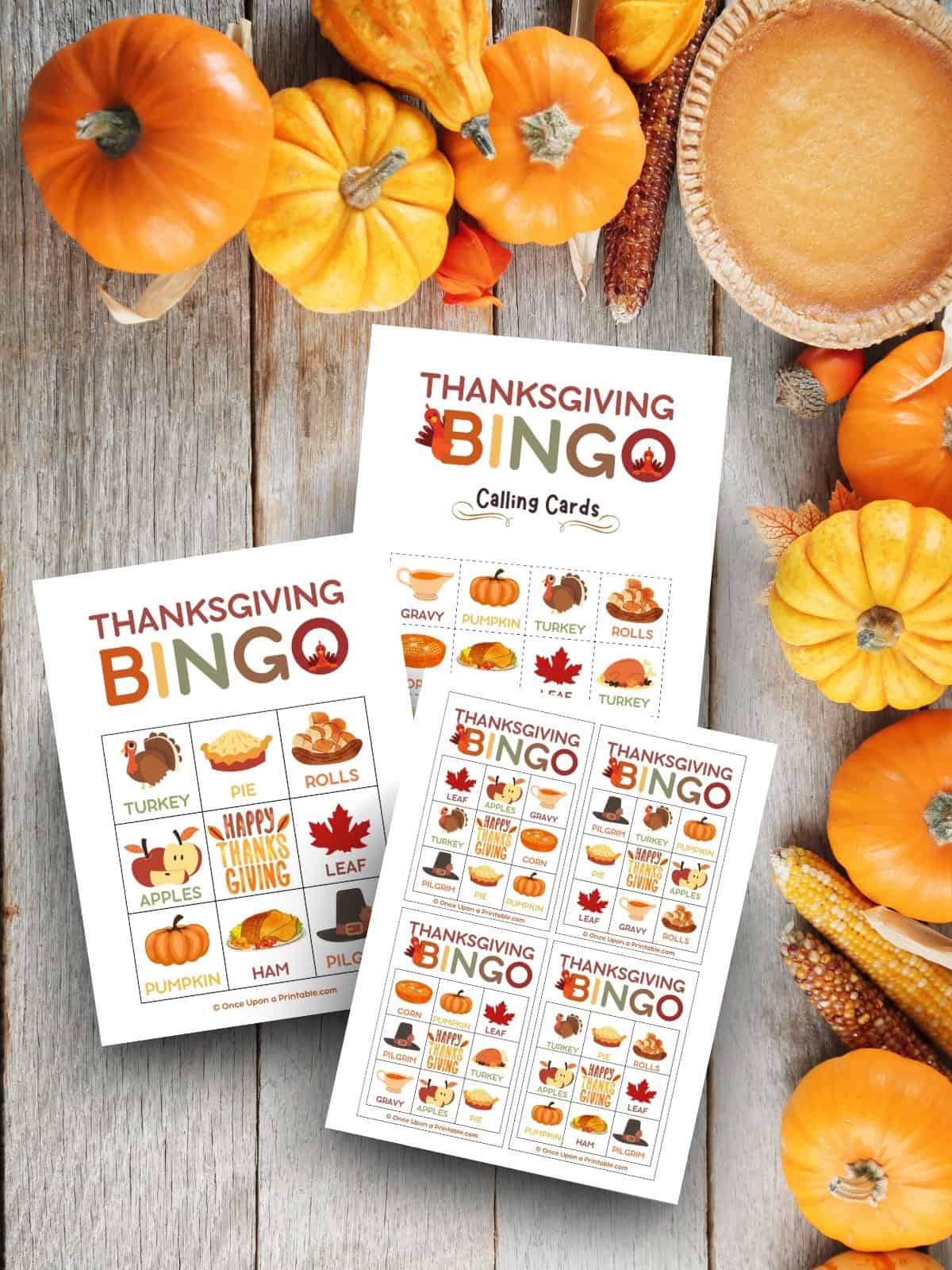 Thanksgiving Bingo cards laying on a wooden background with pumpkins and a pumpkin pie.