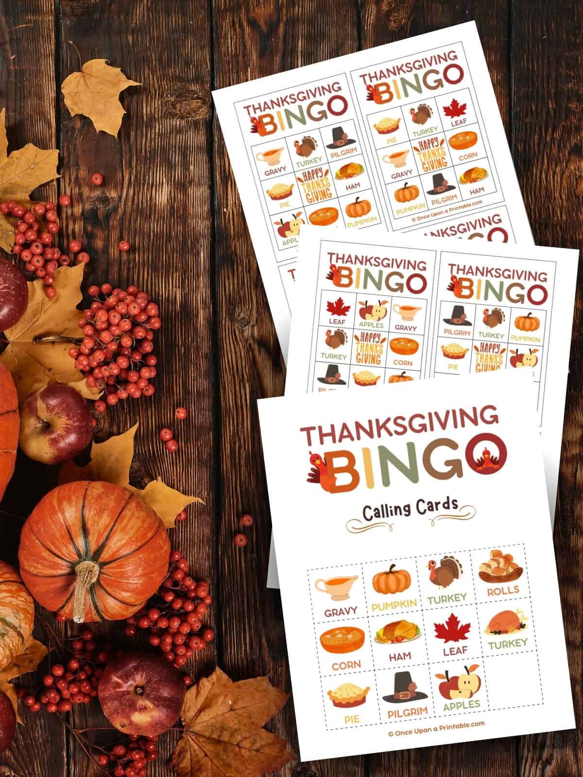 Thanksgiving mini bingo cards and full page of calling cards displayed on a dark wooden background with pumpkins, leaves, and berries.