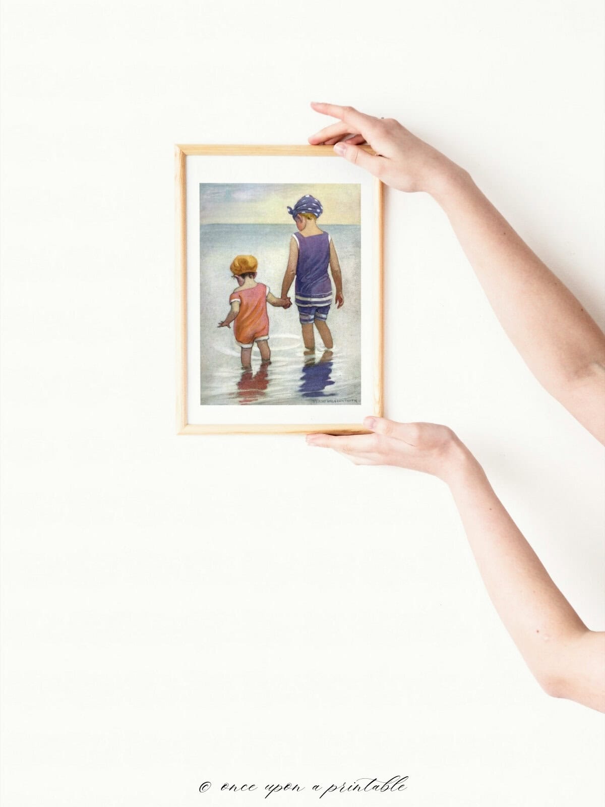 Children in the ocean a vintage illustration framed and held by a woman's hands.