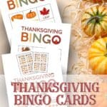 Thanksgiving Bingo cards laying on a peach background with hay and pumpkins.
