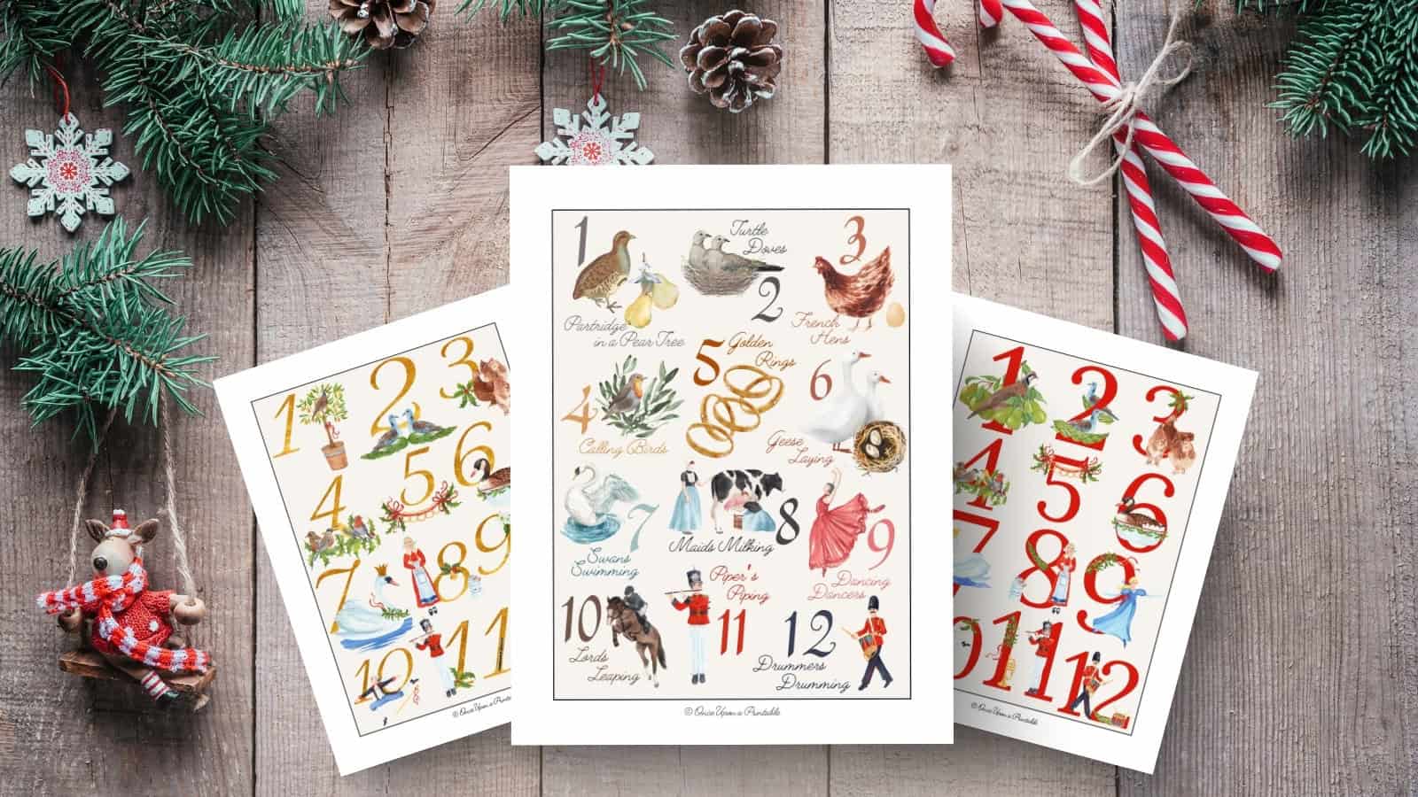 Three full size watercolor art prints of the 12 days of Christmas printed and displayed on a wooden surface with Christmas garland.