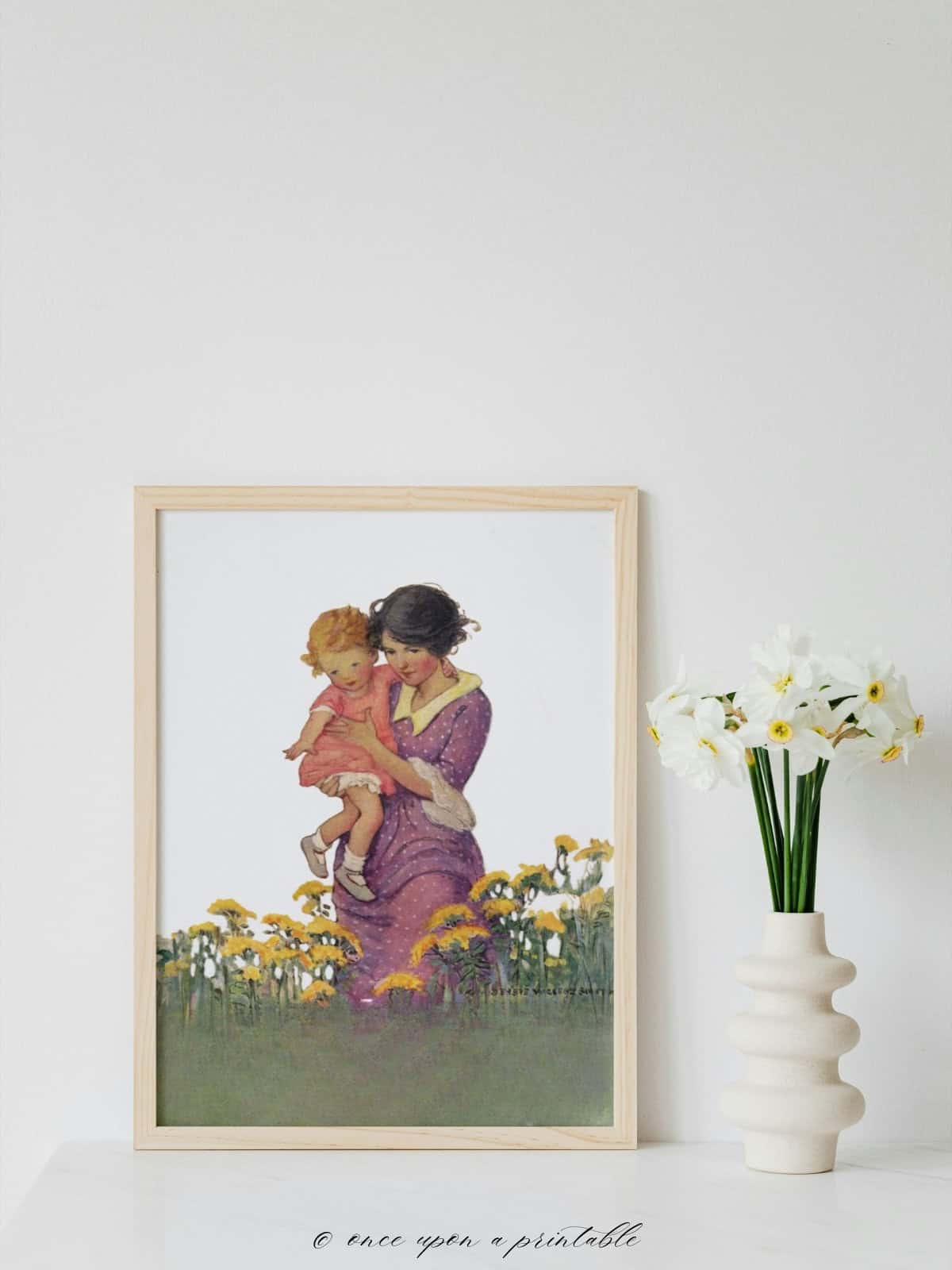 A mother and a little girl in a flower field framed and displayed next to a white vase with daffodils.